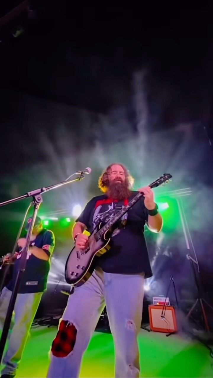Bearded guitarist with long hair performing on stage with green and white stage lighting at Josabi's Live music concert in Helotes, Texas.