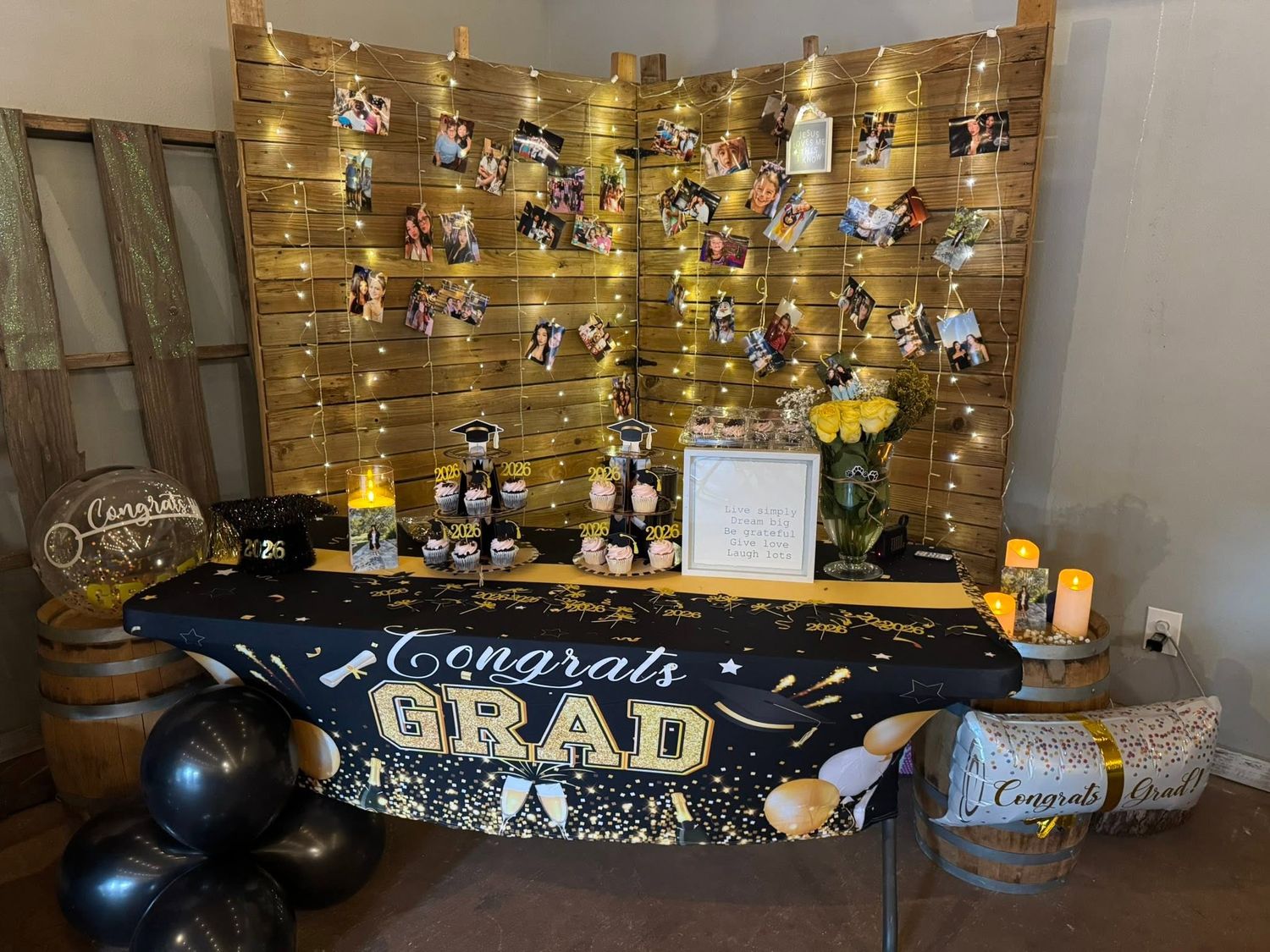 Gold and black graduation table with Congrats Grad banner, photo wall backdrop, balloons, decorative lights at Josabi's Acres in Helotes, TX