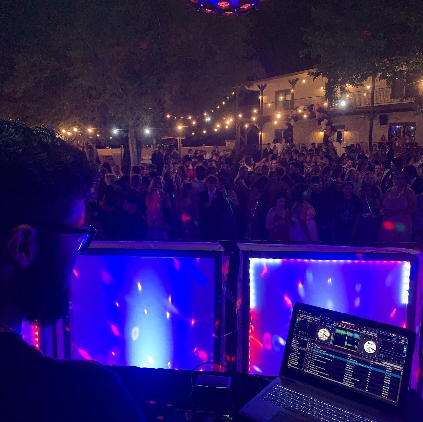 DJ performing at lively outdoor night wedding reception with colorful lights and crowded dance floor at Josabi's Acres in Helotes Texas.