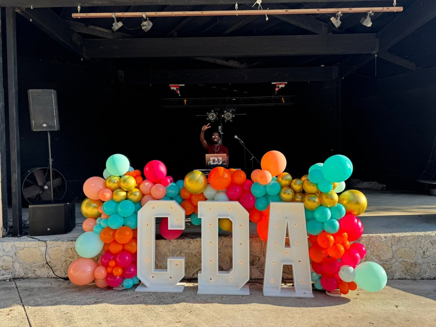 Colorful balloon garland decorating large marquee letters CDA at an outdoor corporate event venue at Josabi's Acres in Helotes, TX.