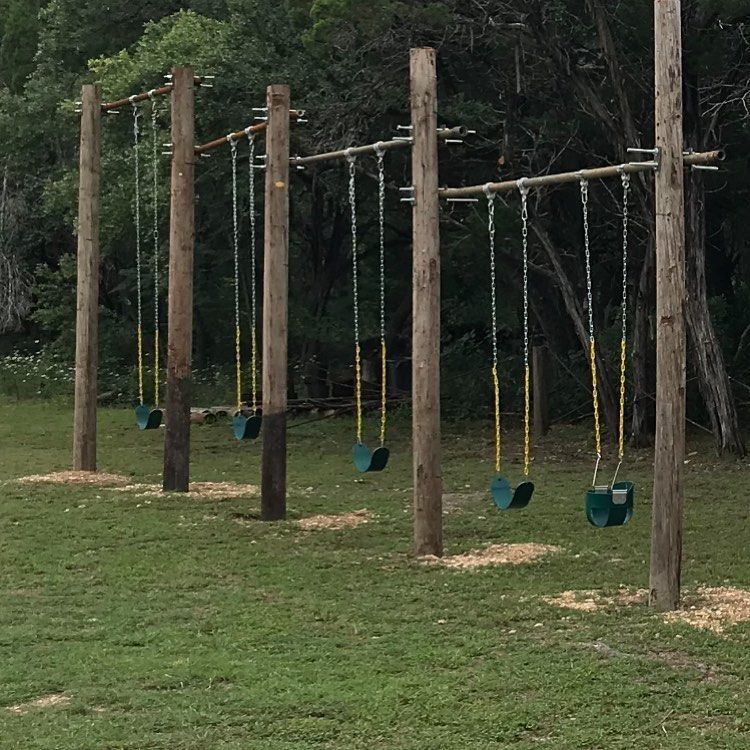 Rustic outdoor playground with wooden post swing set on a green lawn surrounded by trees at Josabi's Acres in Helotes, Texas