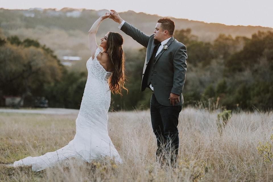 Bride and groom dancing in golden field at sunset, groom spinning bride in white lace wedding dress at Josabi's Acres in Helotes Texas.