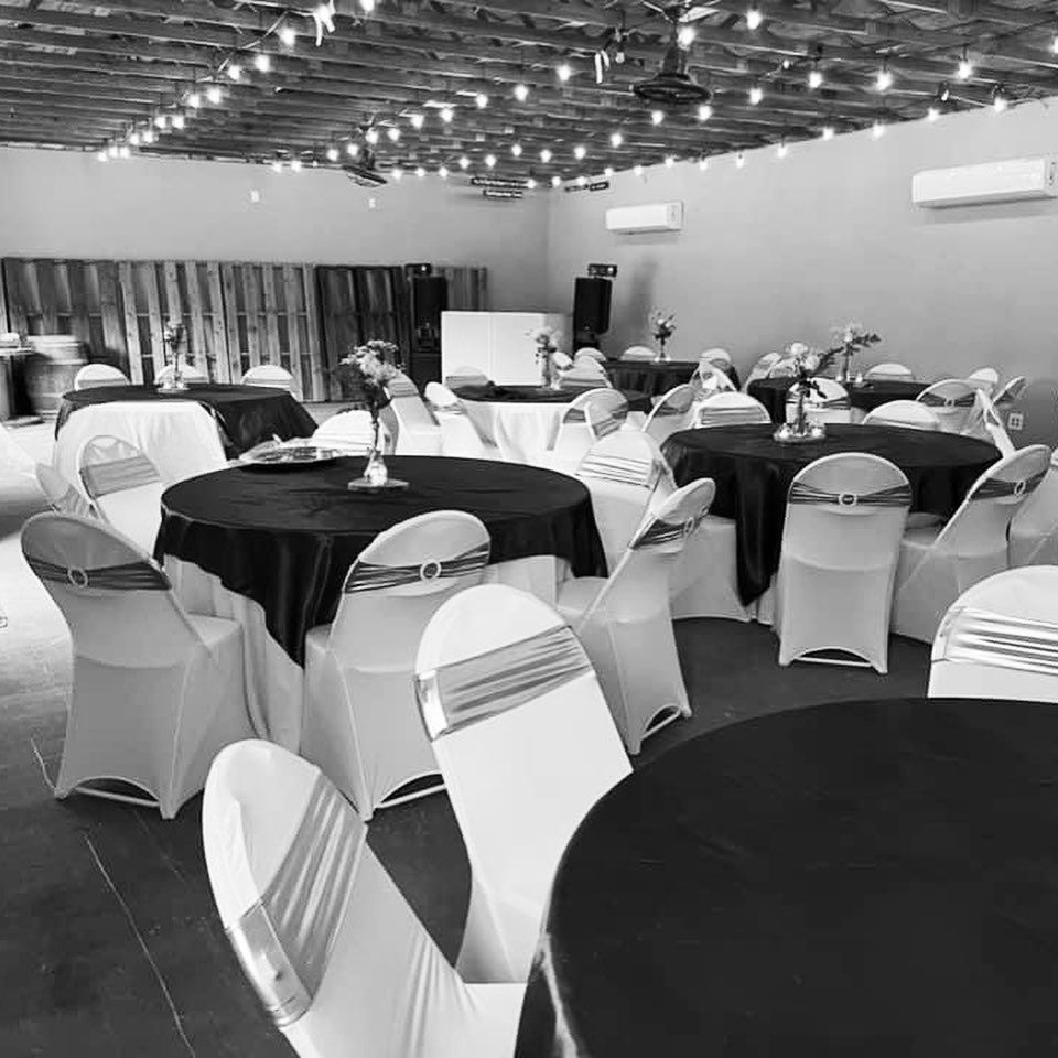 Black and white photo of elegant event venue interior with round tables and white chair covers at Josabi's Acres in Helotes, Texas.