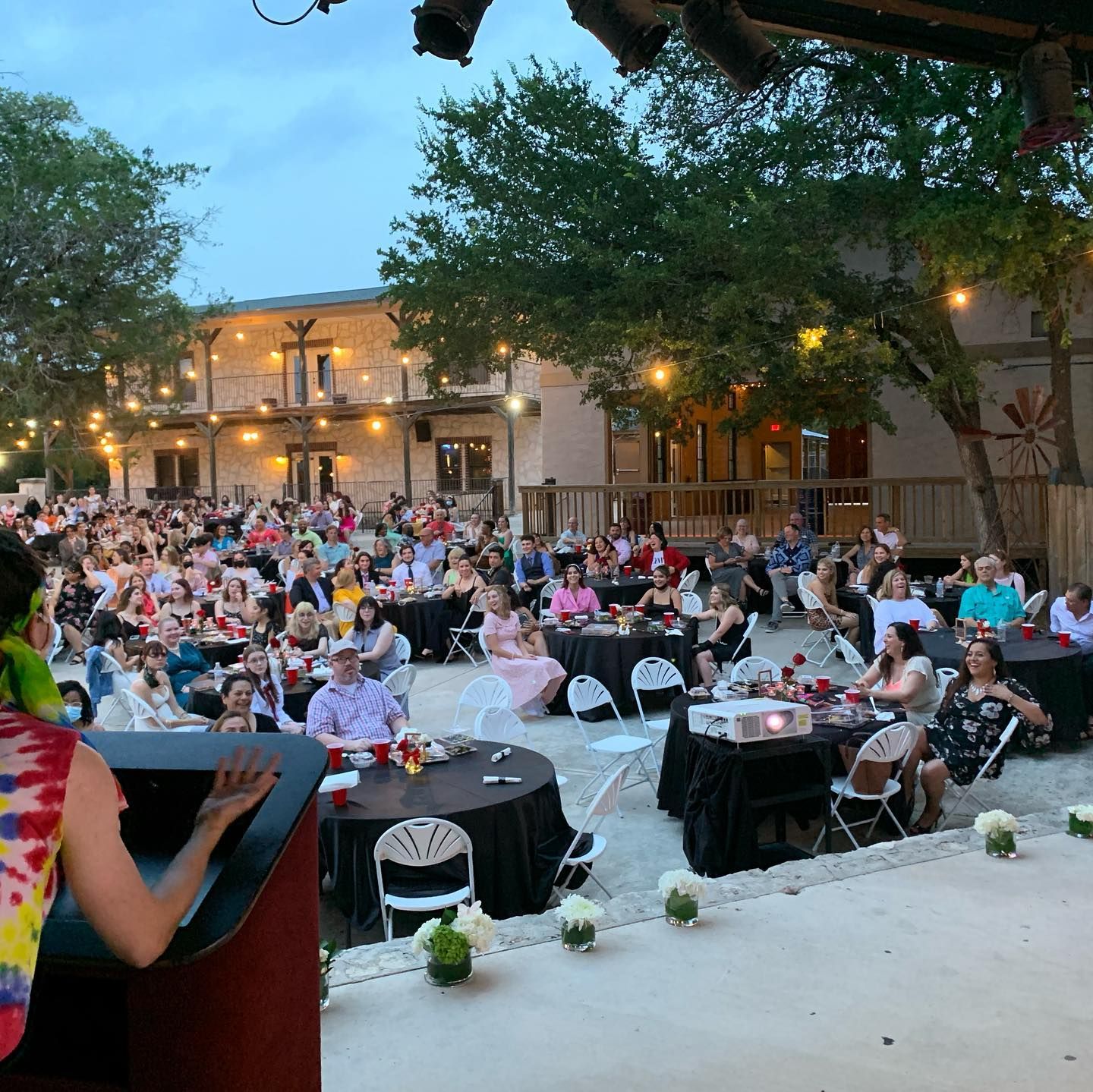 Large outdoor evening event with guests seated at black-draped tables under string lights at Josabi's Acres in Helotes Texas.