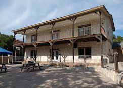 Historic two-story stone building with wooden balcony, picnic tables at Josabi's Acres in Helotes, Texas.