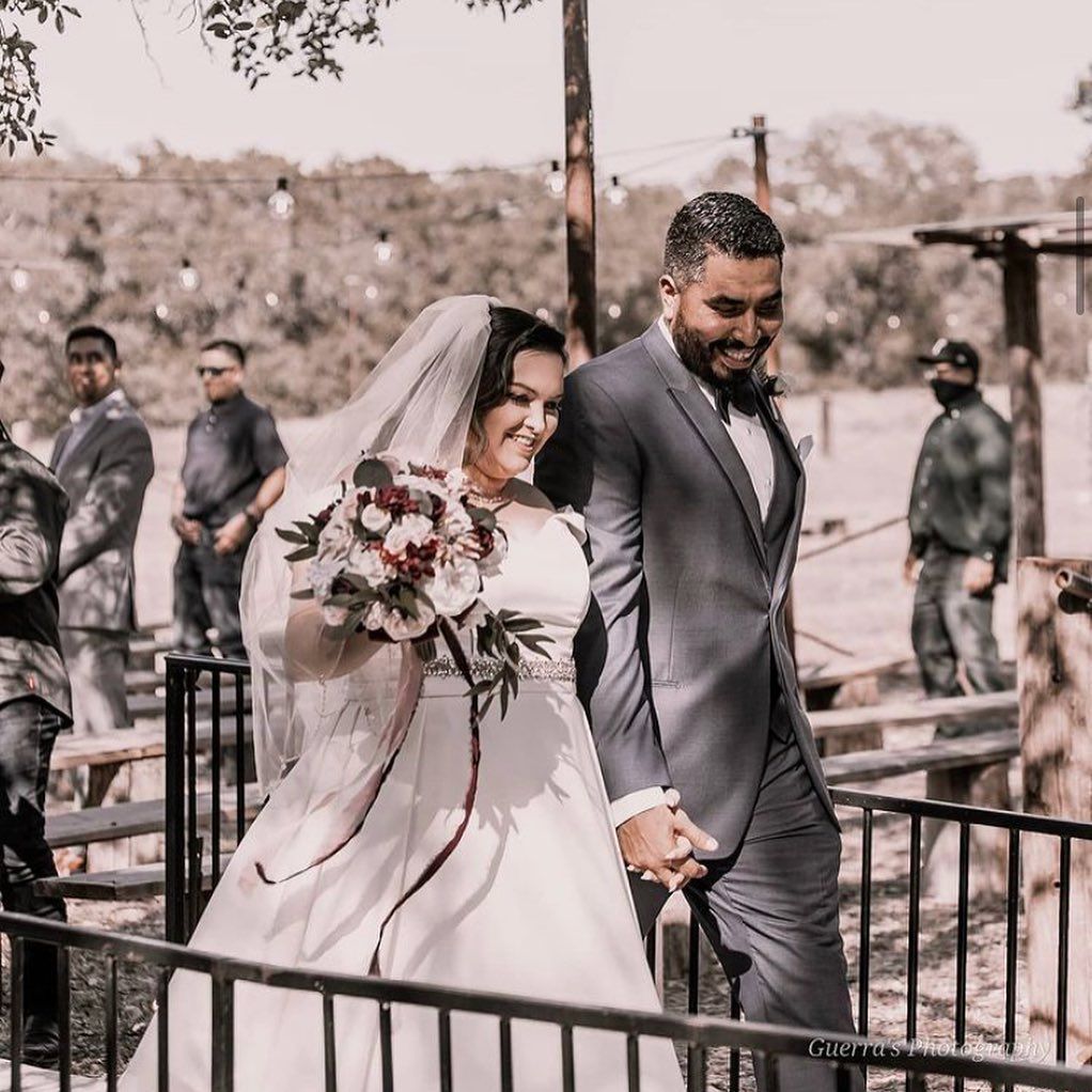 Bride in white gown with bouquet and groom in gray suit walk hand in hand at outdoor wedding at Josabi's Acres in Helotes Texas.