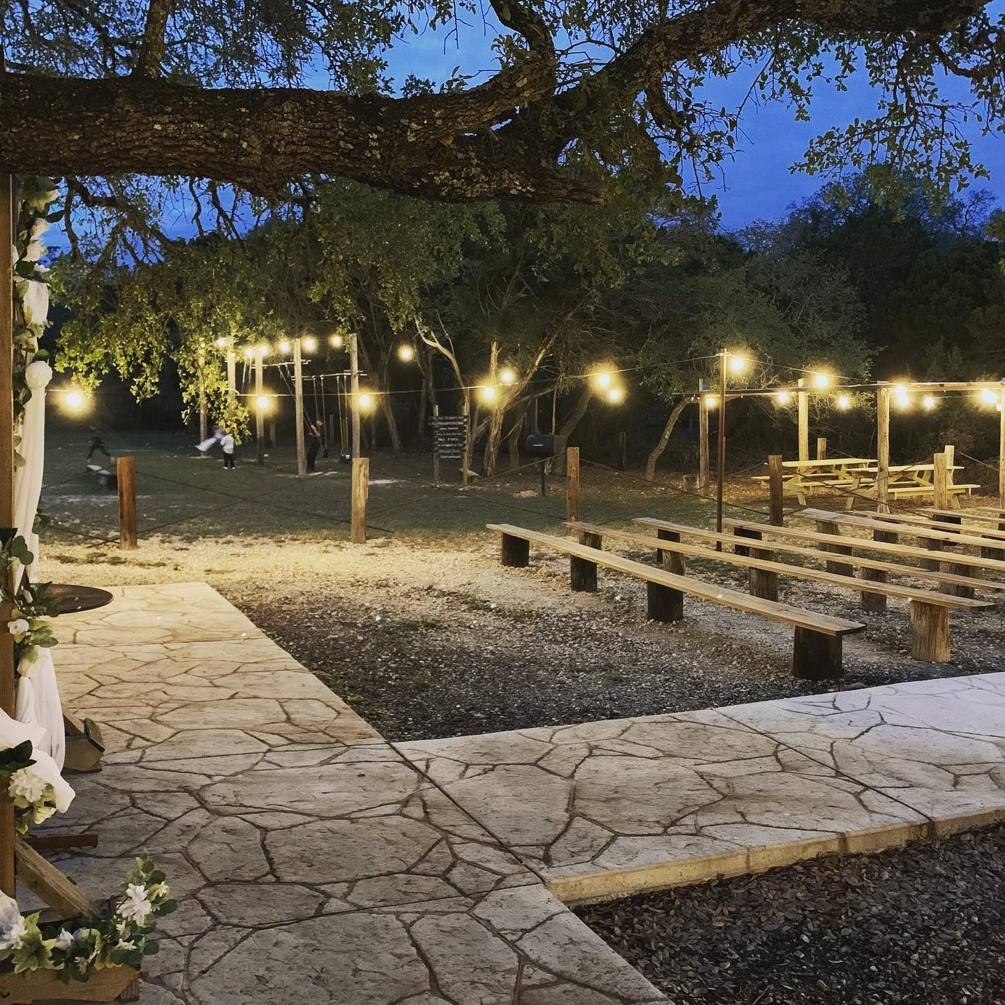 Elegant outdoor wedding venue at dusk with stone pathway, wooden benches, and warm string lights at Josabi's Acres in Helotes, Texas.