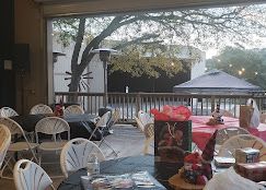 Indoor and outdoor dining area with white chairs, red tablecloths, gazebo, and tree views at Josabi's Acres in Helotes, Texas