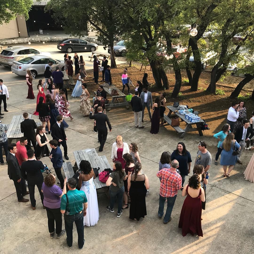 Aerial view of wedding guests mingling outdoors on a concrete patio surrounded by oak trees at Josabi's Acres in Helotes, Texas