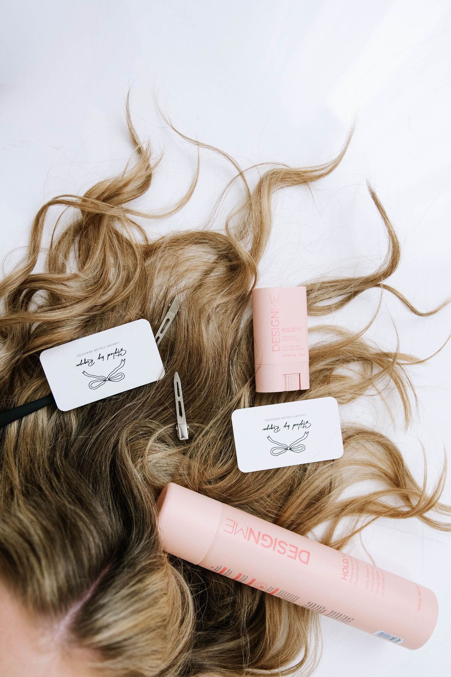 Wavy blonde hair extensions with clips and Designme hair products arranged on white surface.   Photography Studio in Bartow Florida