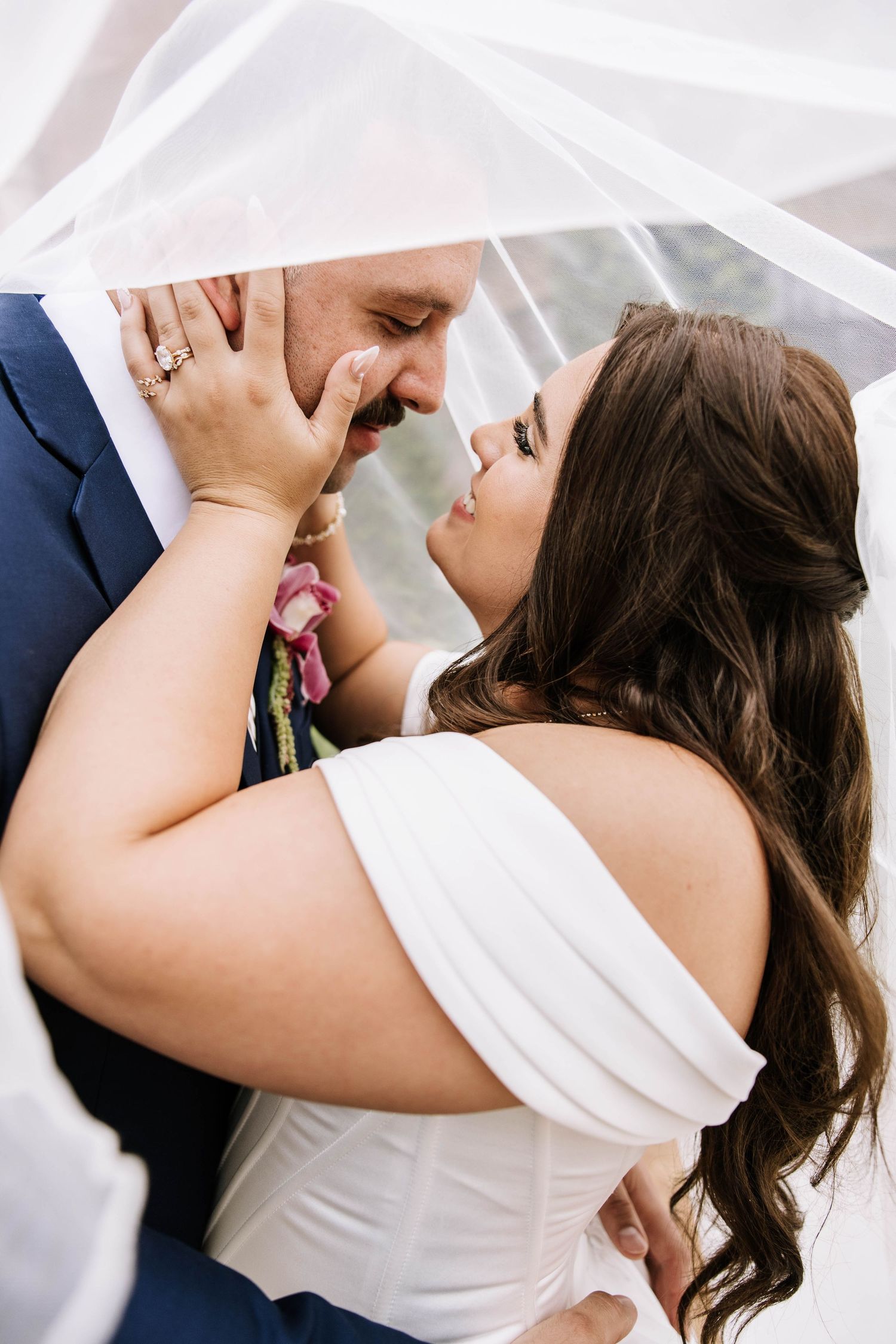 Romantic close-up of bride and groom almost kissing under a flowing white veil.
