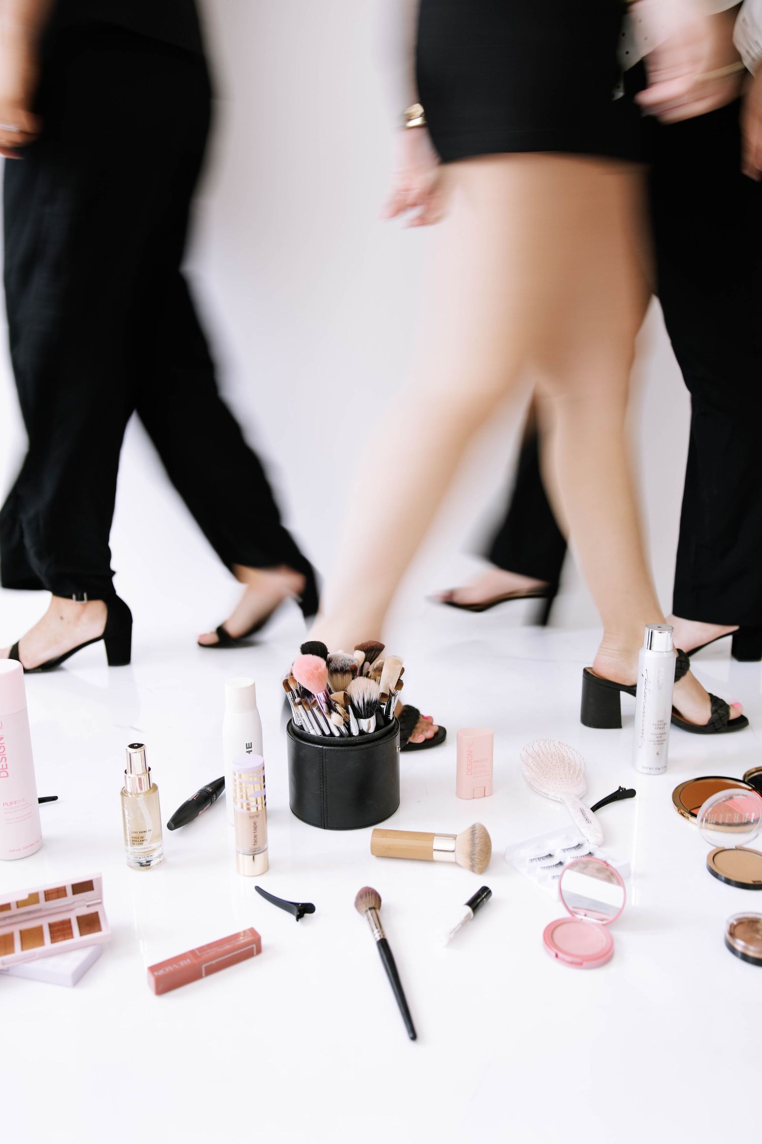 Makeup brushes and cosmetics displayed on a white floor with women in black outfits walking behind.