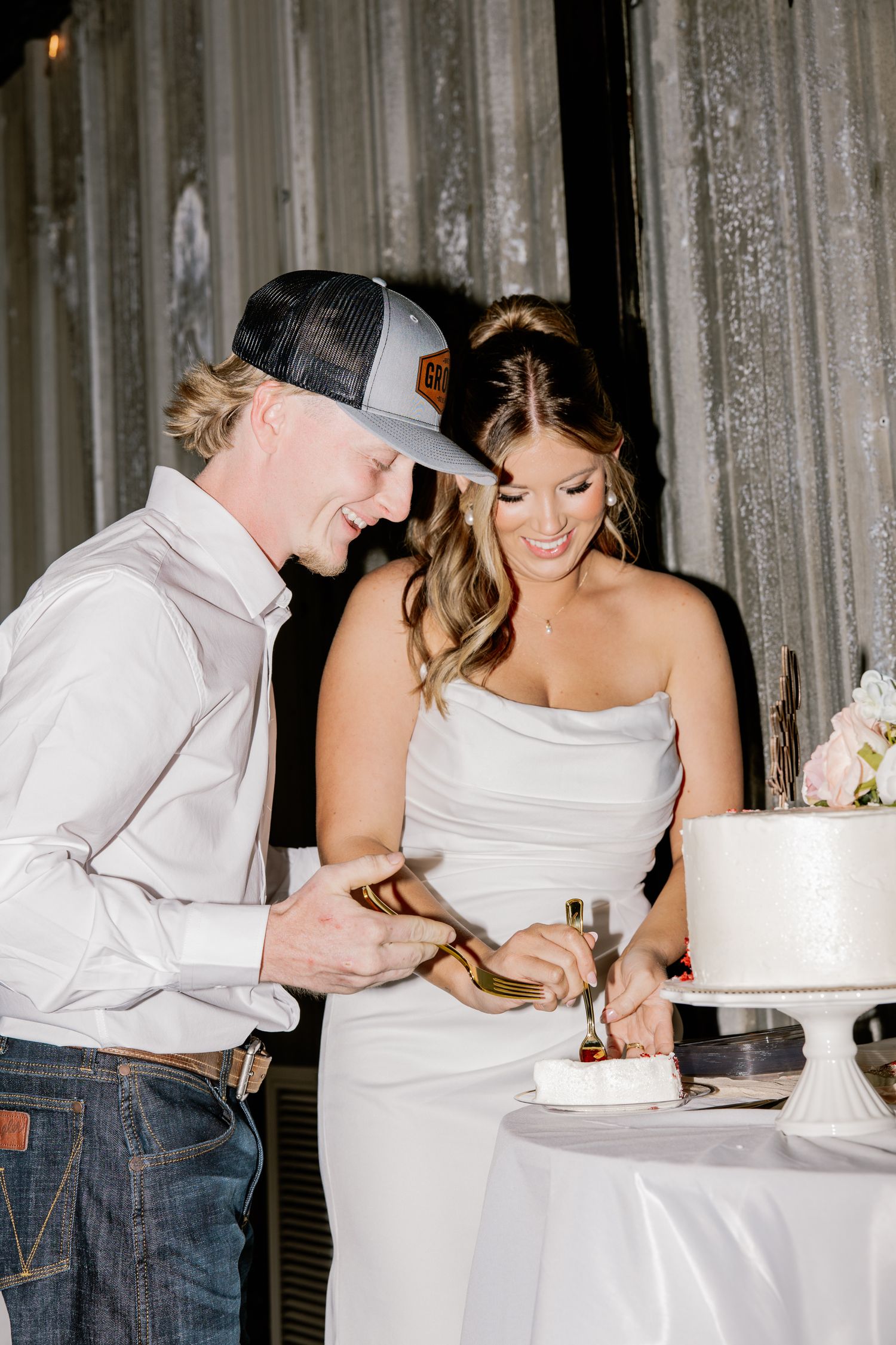 Smiling bride in white gown and groom in cap cut wedding cake together at elegant reception.