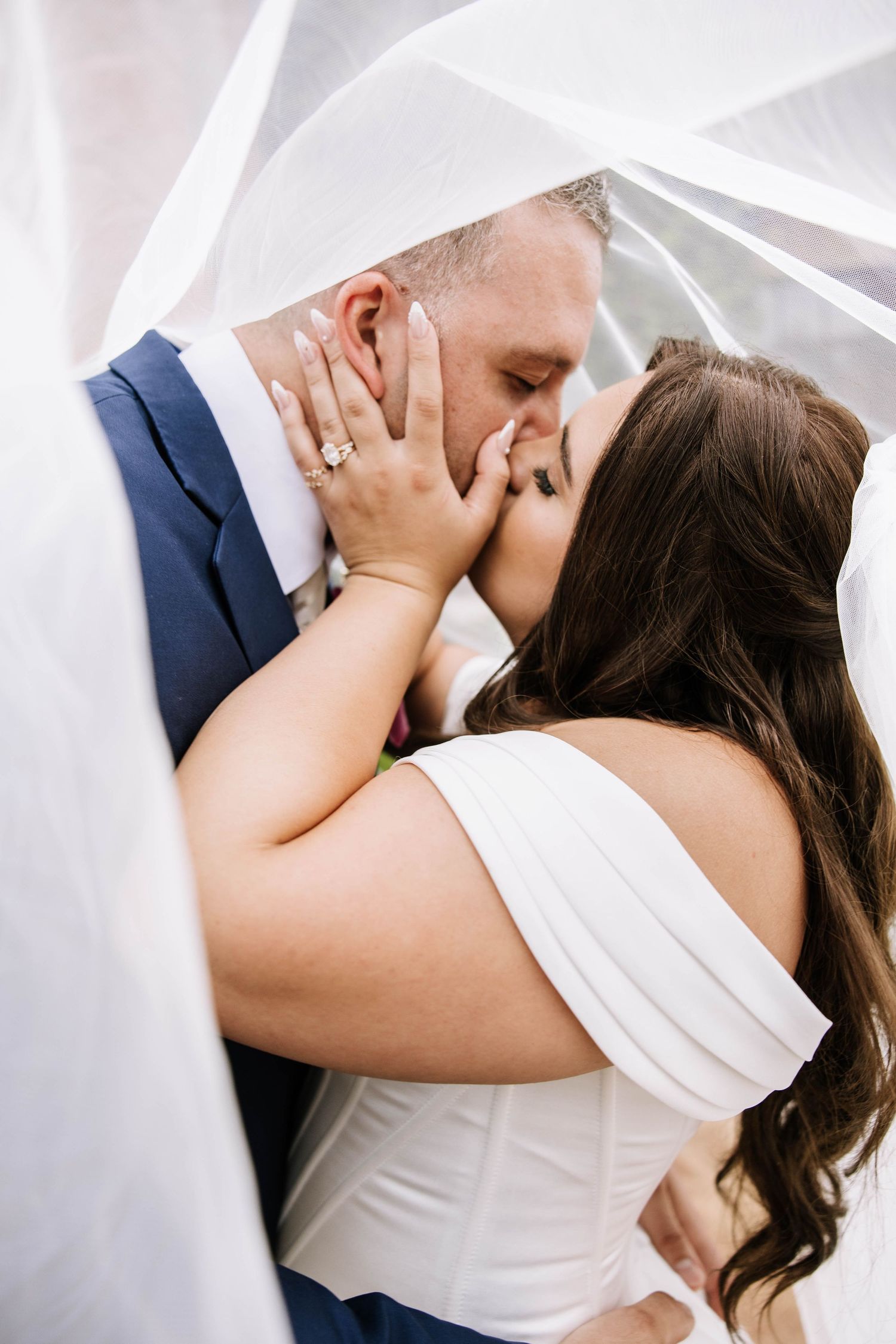 Bride and groom sharing a kiss under a flowing white veil outdoors.