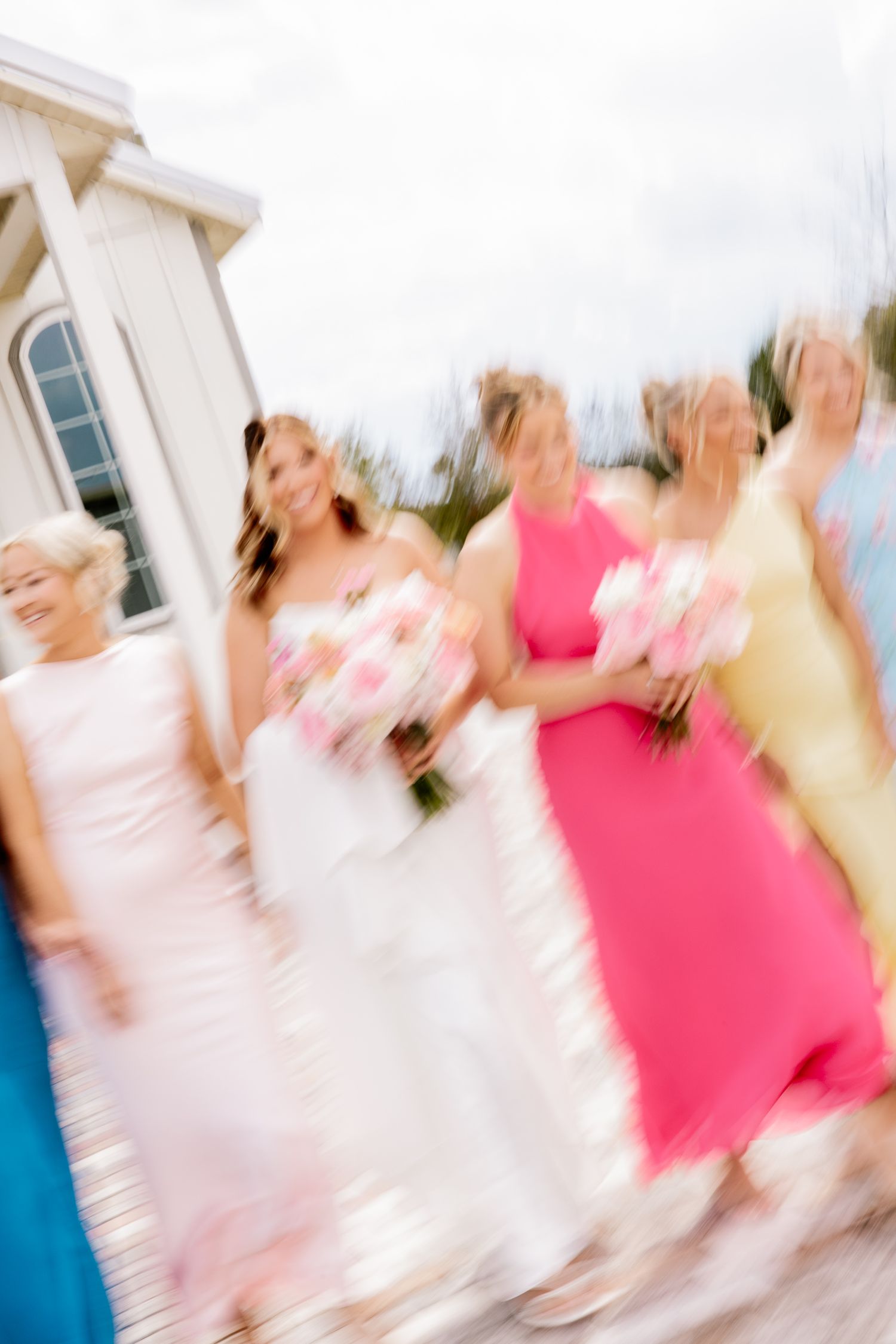 Blurred motion shot of bride and bridesmaids in colorful gowns walking together outdoors.