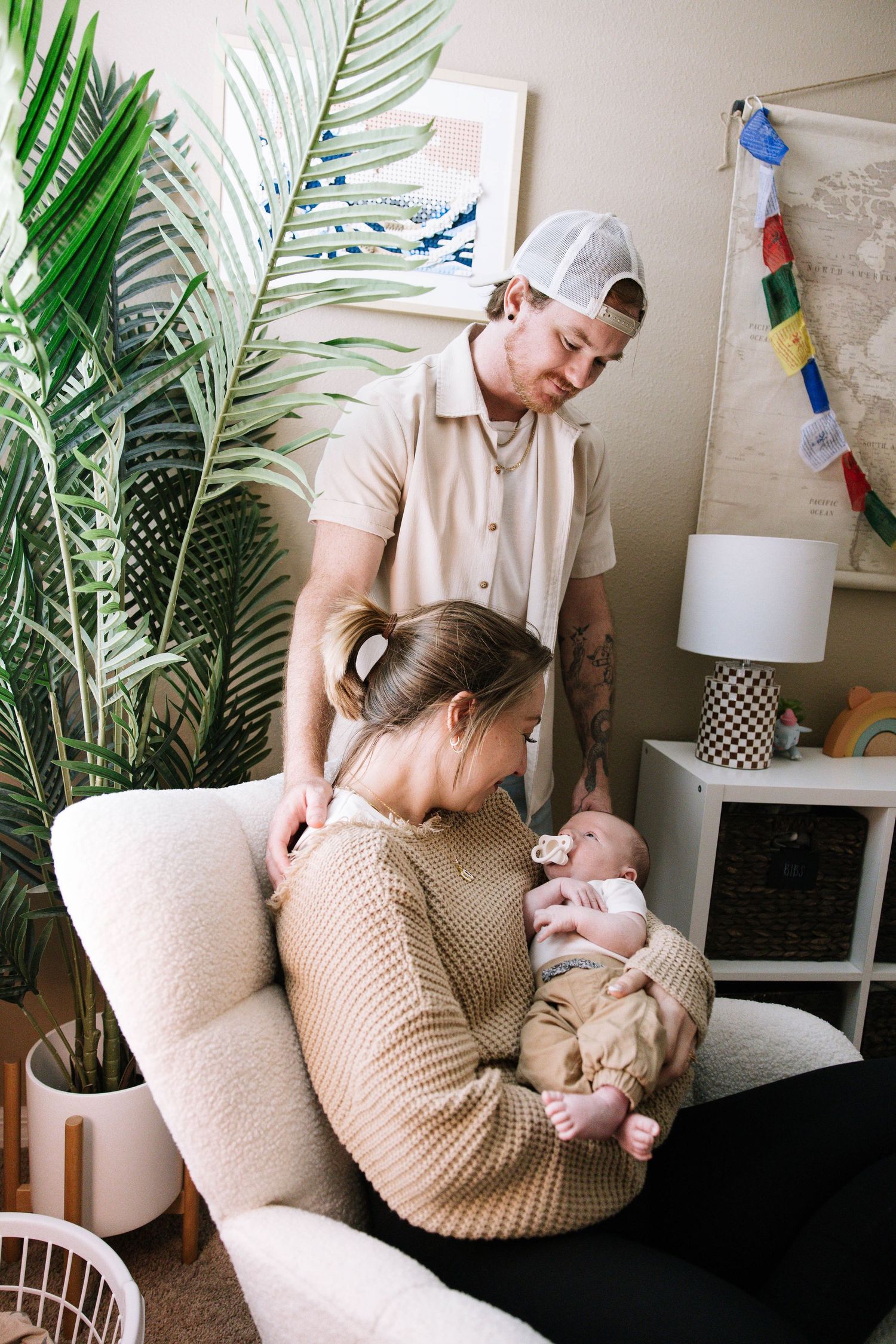 Father in white cap watches lovingly as mother holds newborn baby in a bohemian-styled nursery. Home in Lakeland Florida.
