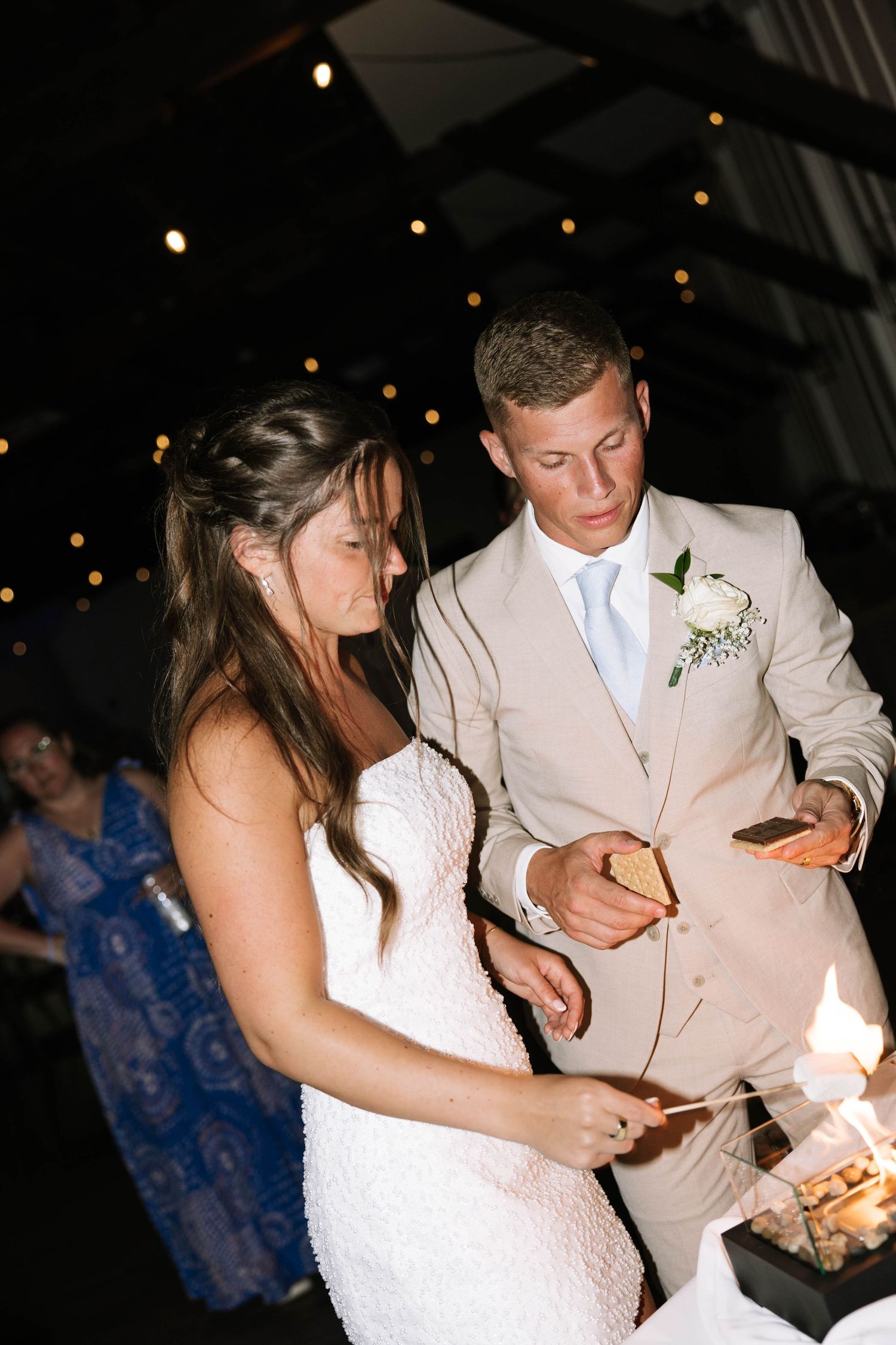 Bride and groom in tan suit light sparkler at outdoor night reception.