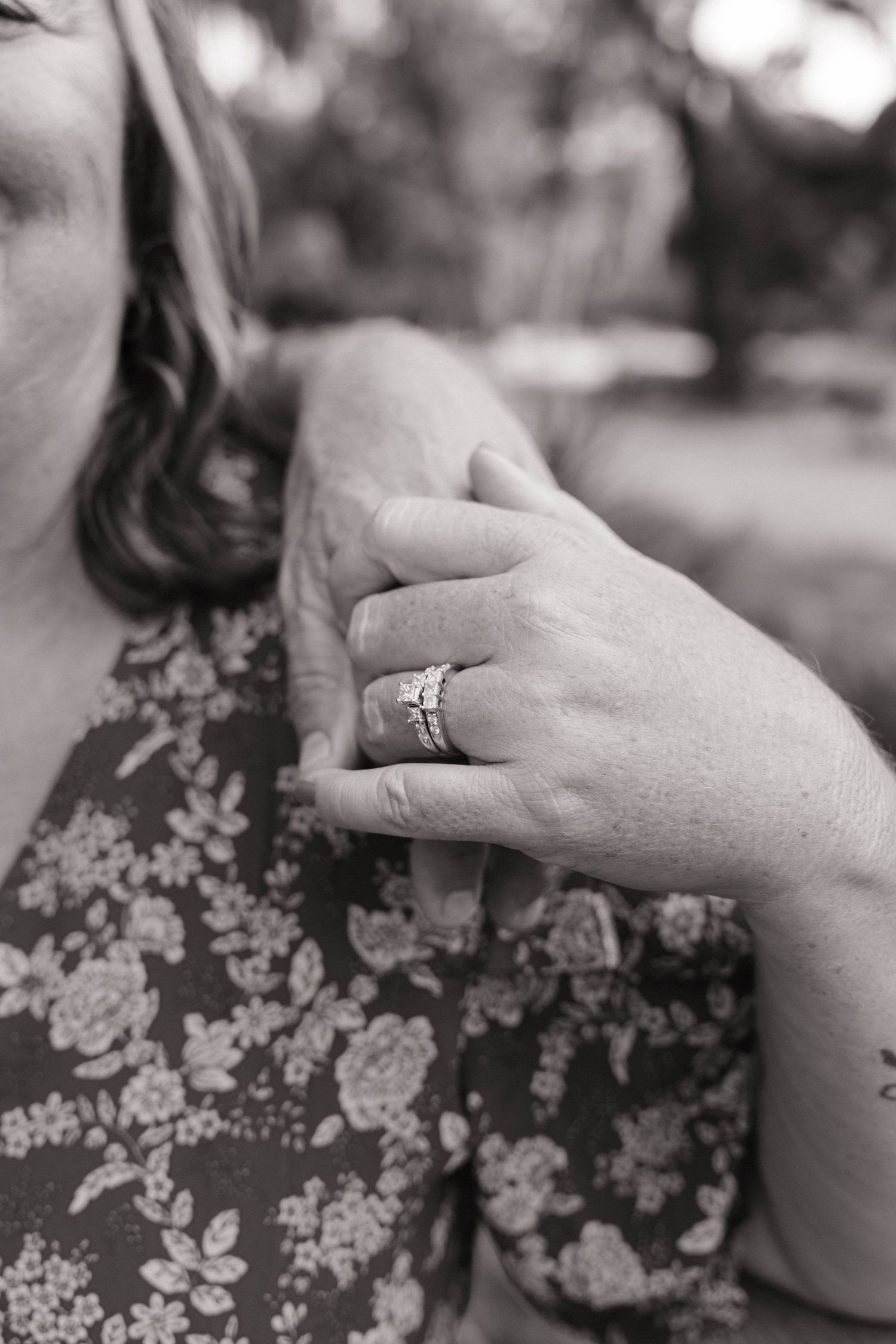 Close-up black and white photo of a woman's hand displaying a diamond engagement ring and wedding band.