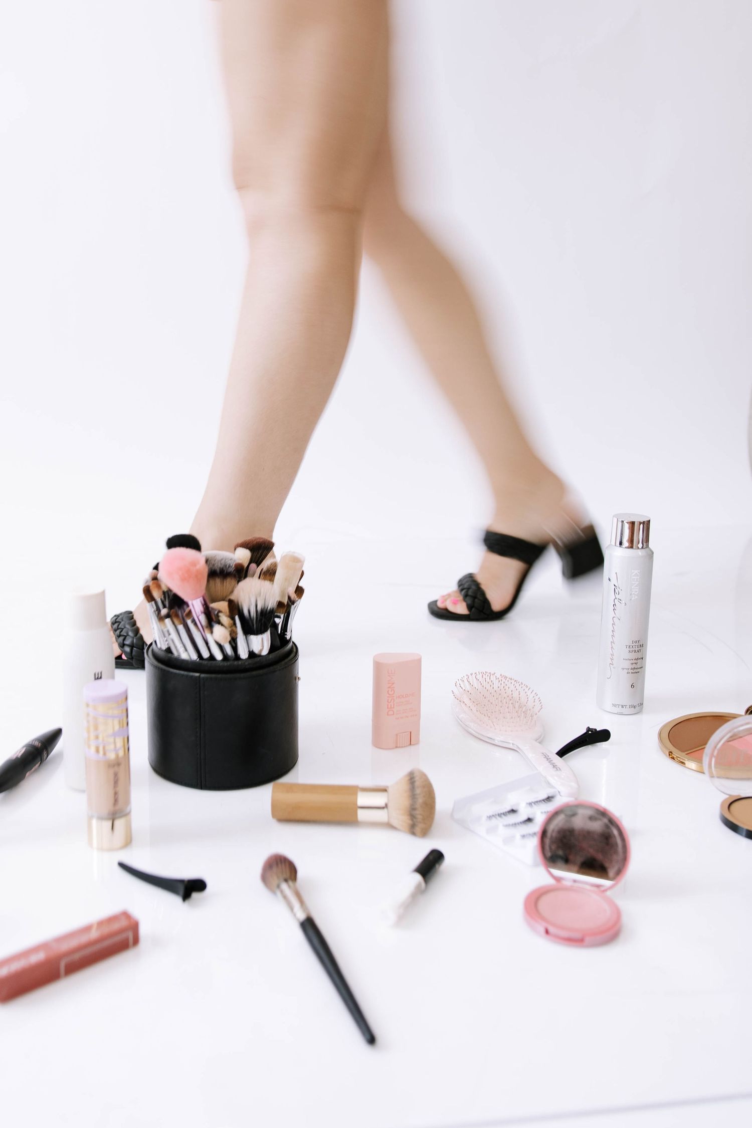 Close-up of makeup brushes and beauty products spread on white floor with womans legs in heels.Photography Studio in Bartow Florida.