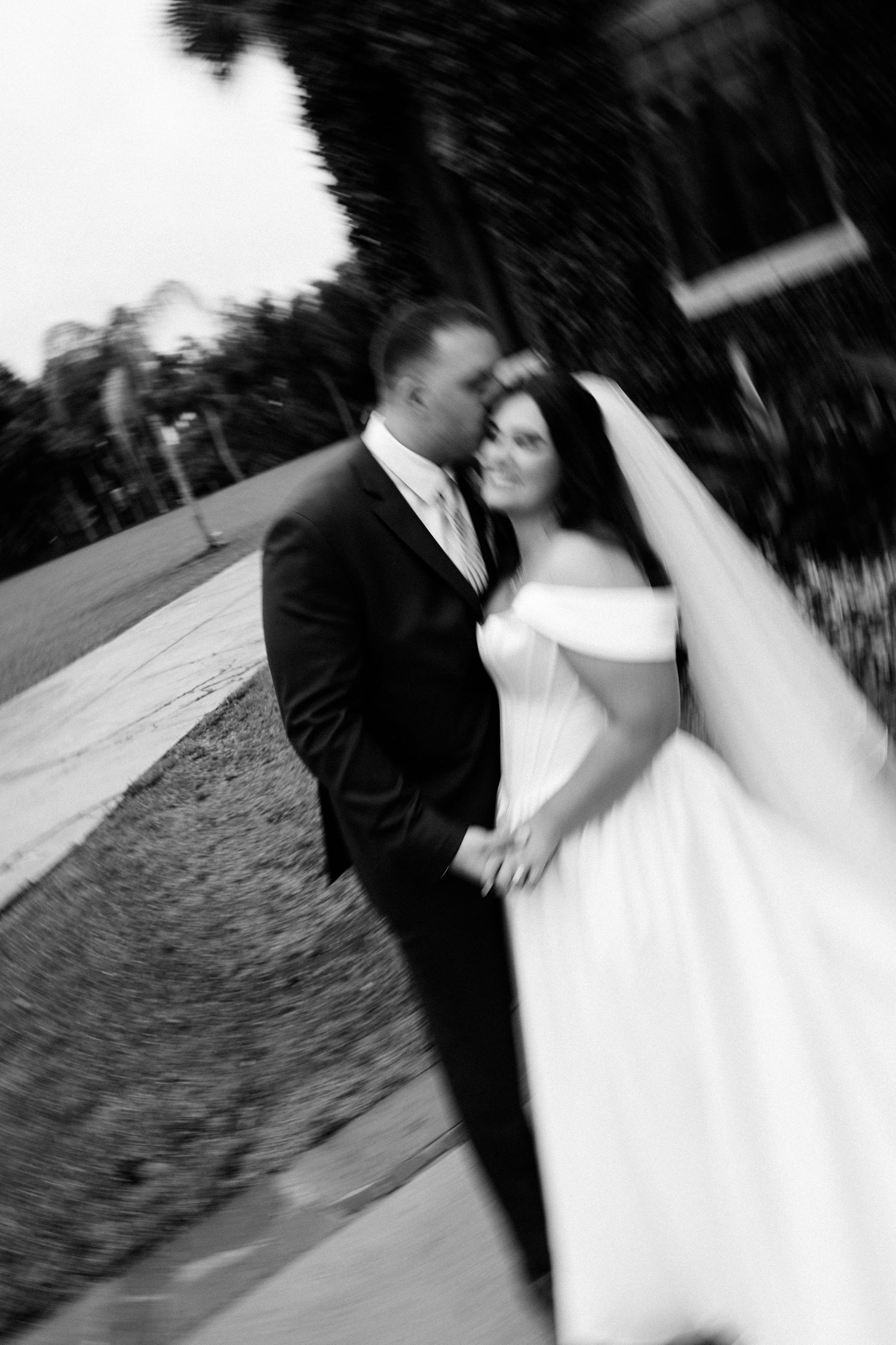 Black and white photo of a bride and groom holding hands and sharing a romantic moment outdoors on their wedding day.