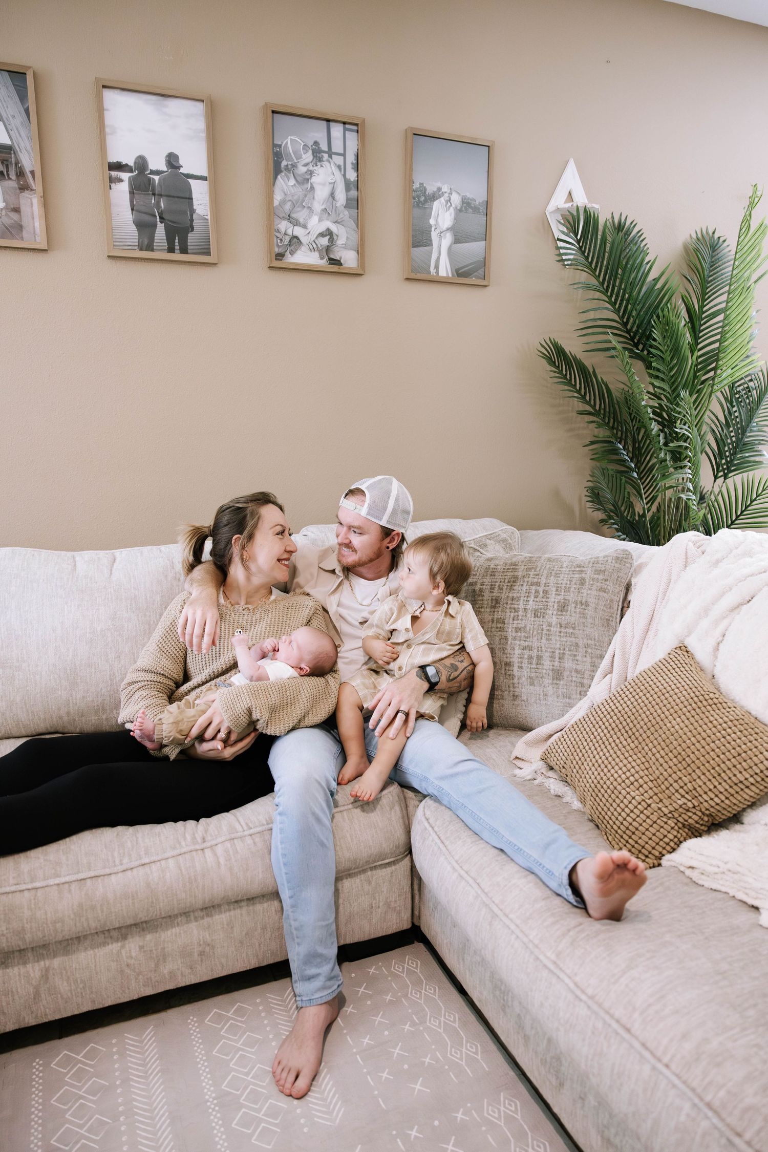 Happy family with newborn and toddler sitting together on a beige sectional sofa in cozy living room. Home in Lakeland Florida.