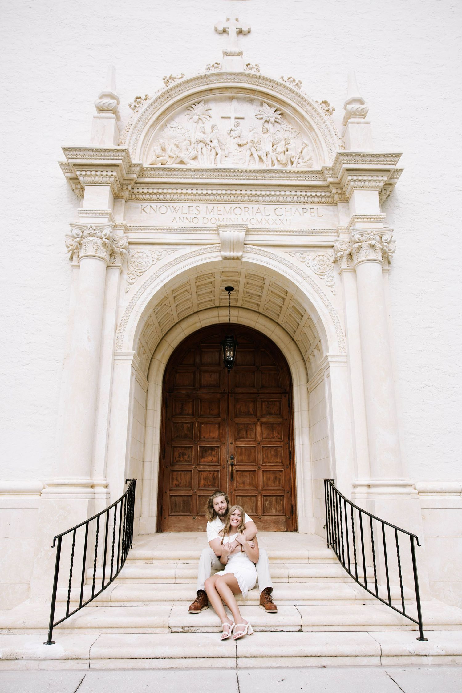 Couple sitting together on steps of an ornate white church entrance.
