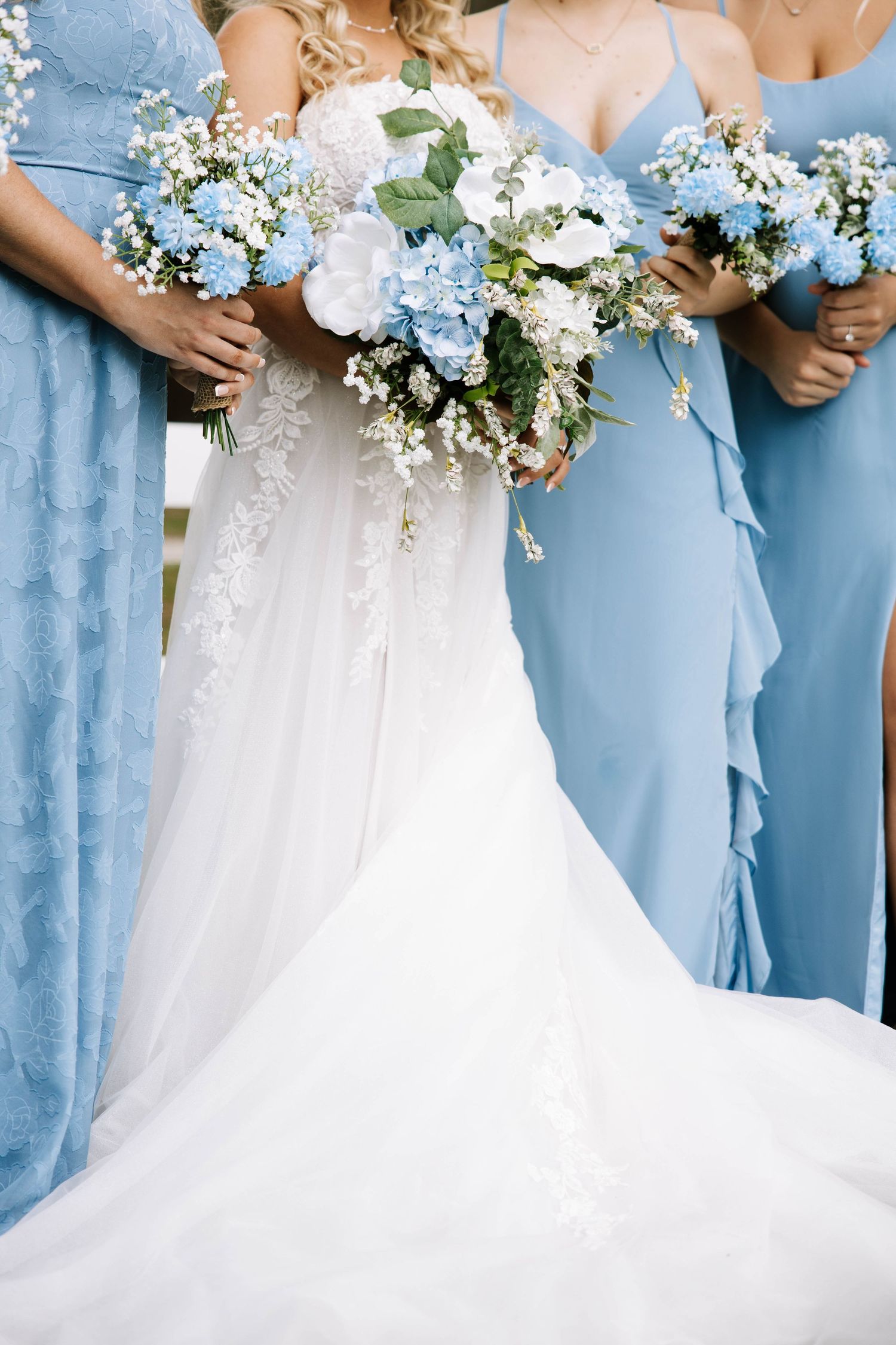 Bride and bridesmaids in blue dresses holding bouquets of blue hydrangeas and white flowers.