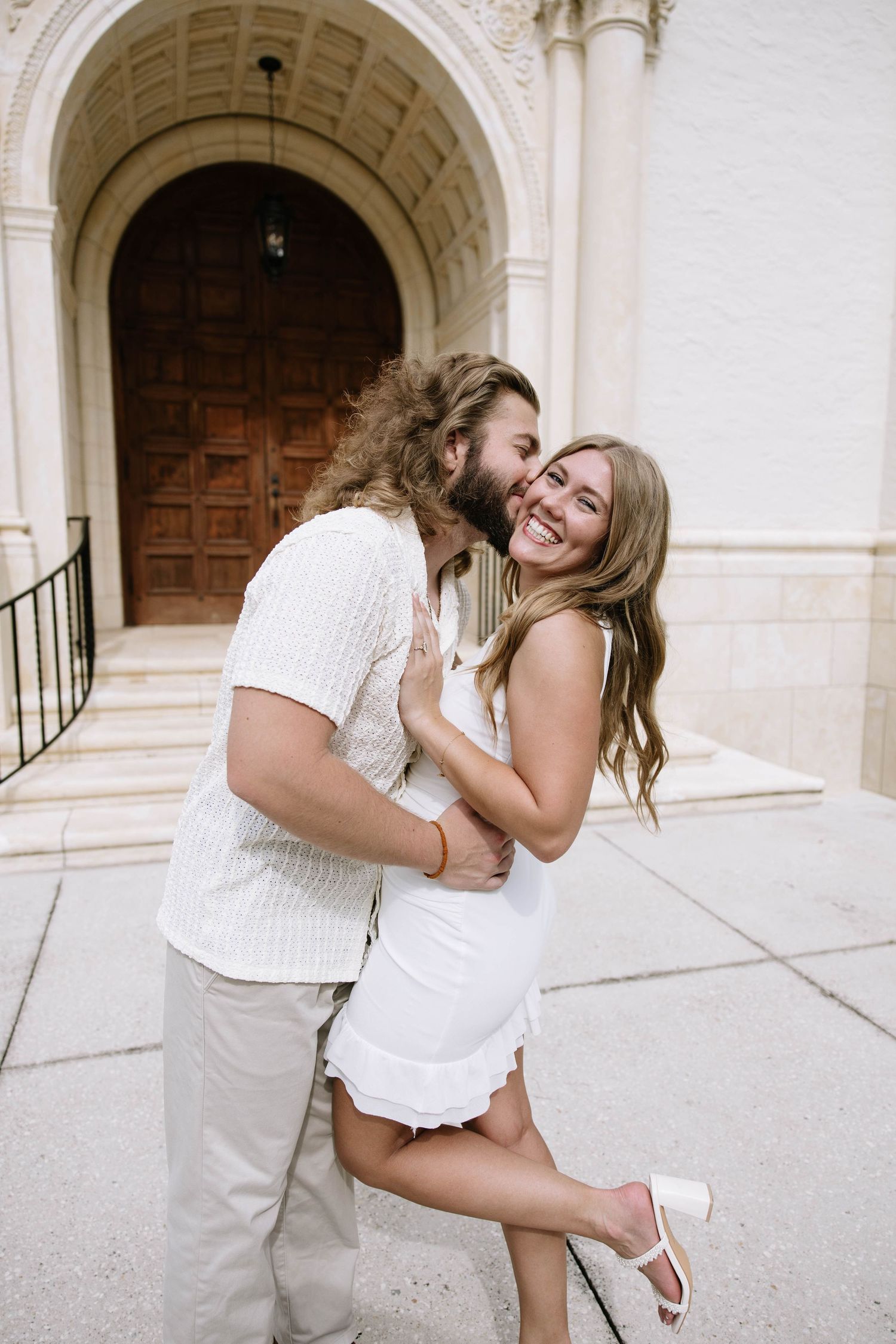 Couple laughing and embracing outside ornate church archway during engagement session.