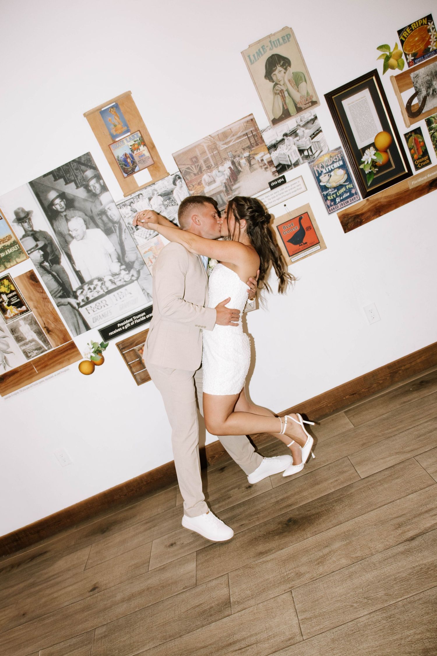 Couple sharing a kiss in a casual elopement setting with vintage posters on white wall.