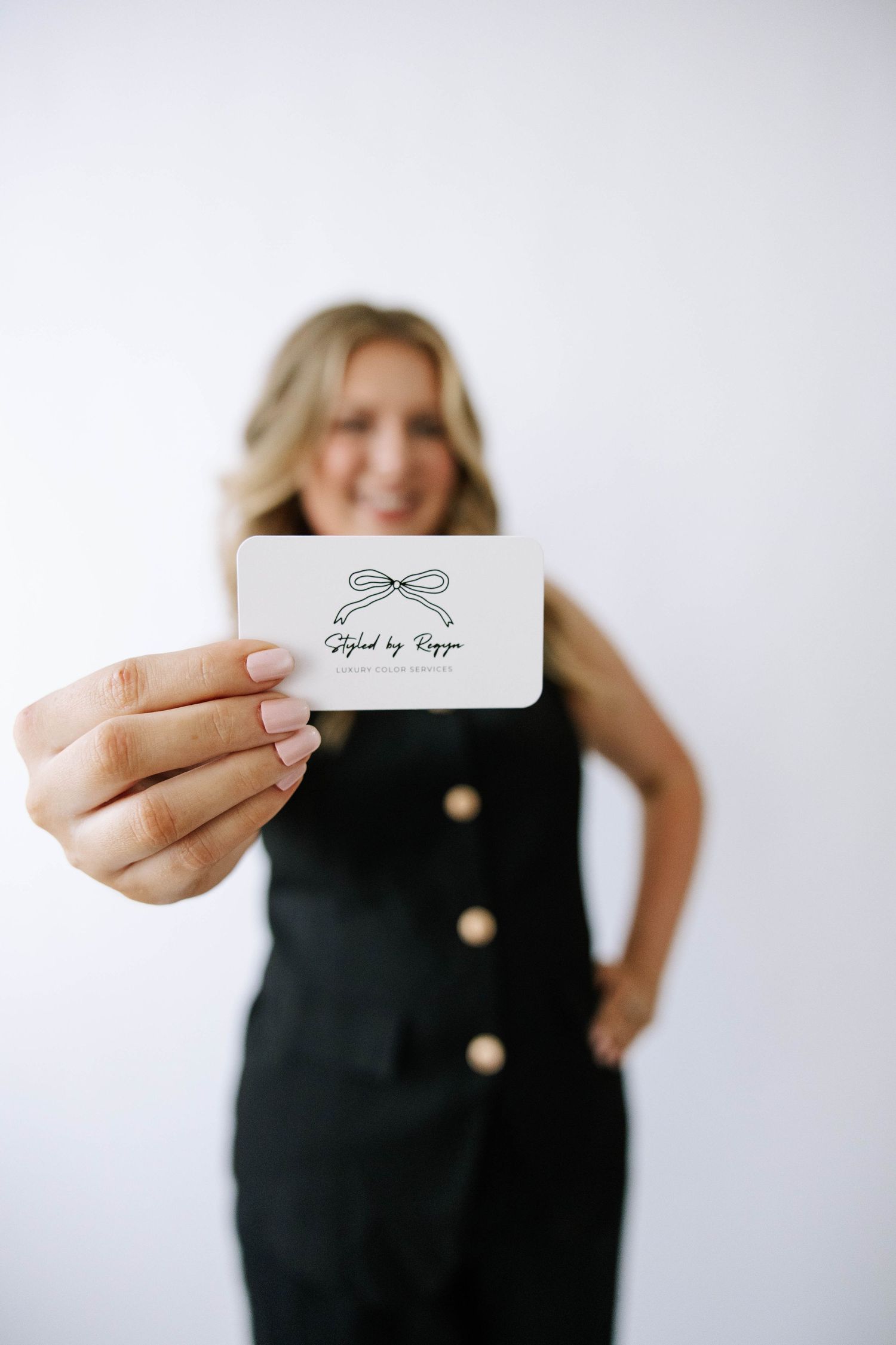 Smiling blonde woman holds business card reading Styled by Reggie with bow logo in foreground. Bartow Florida