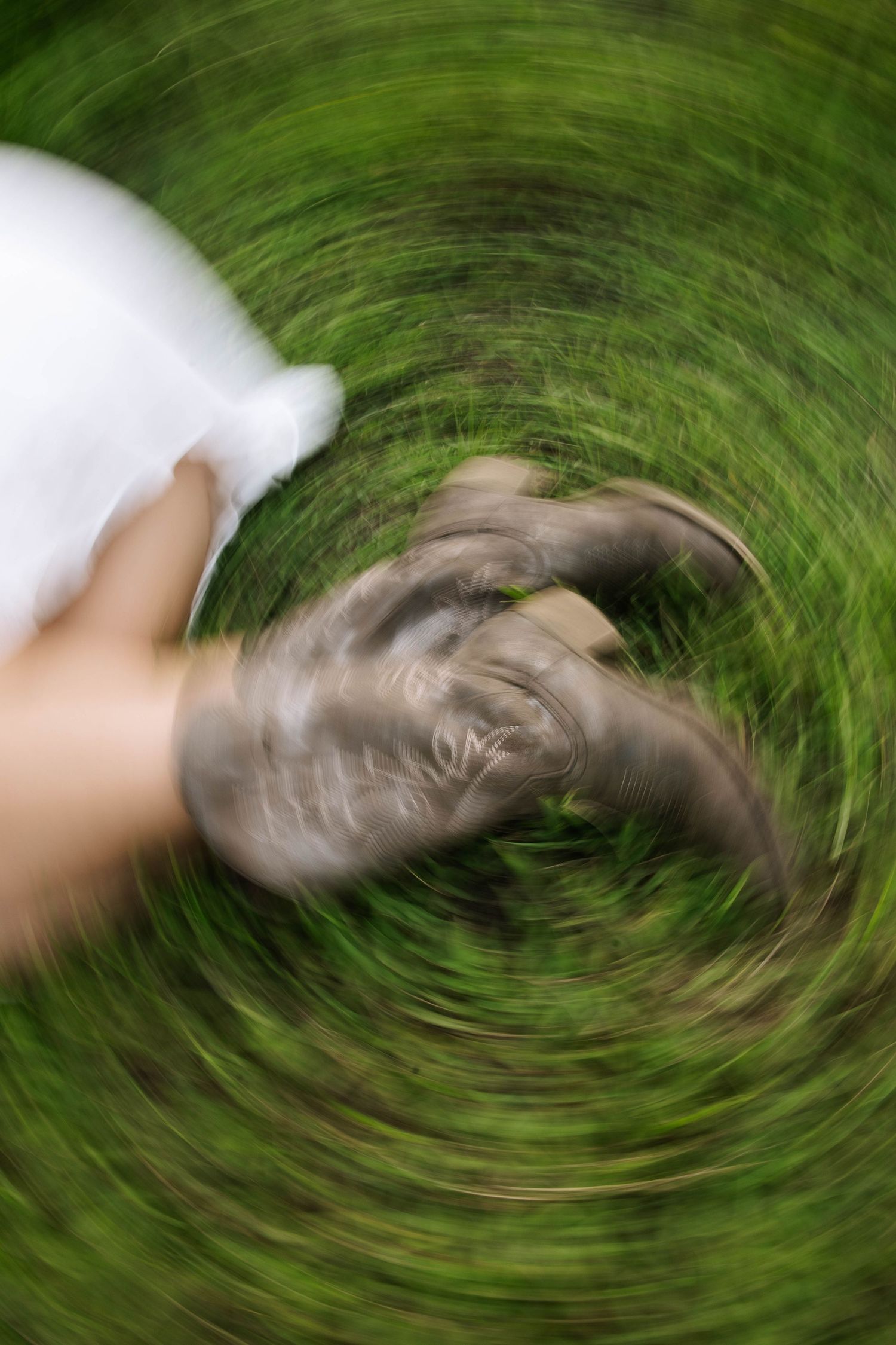 Spinning motion blur photo of person in white dress and cowboy boots standing on green grass.