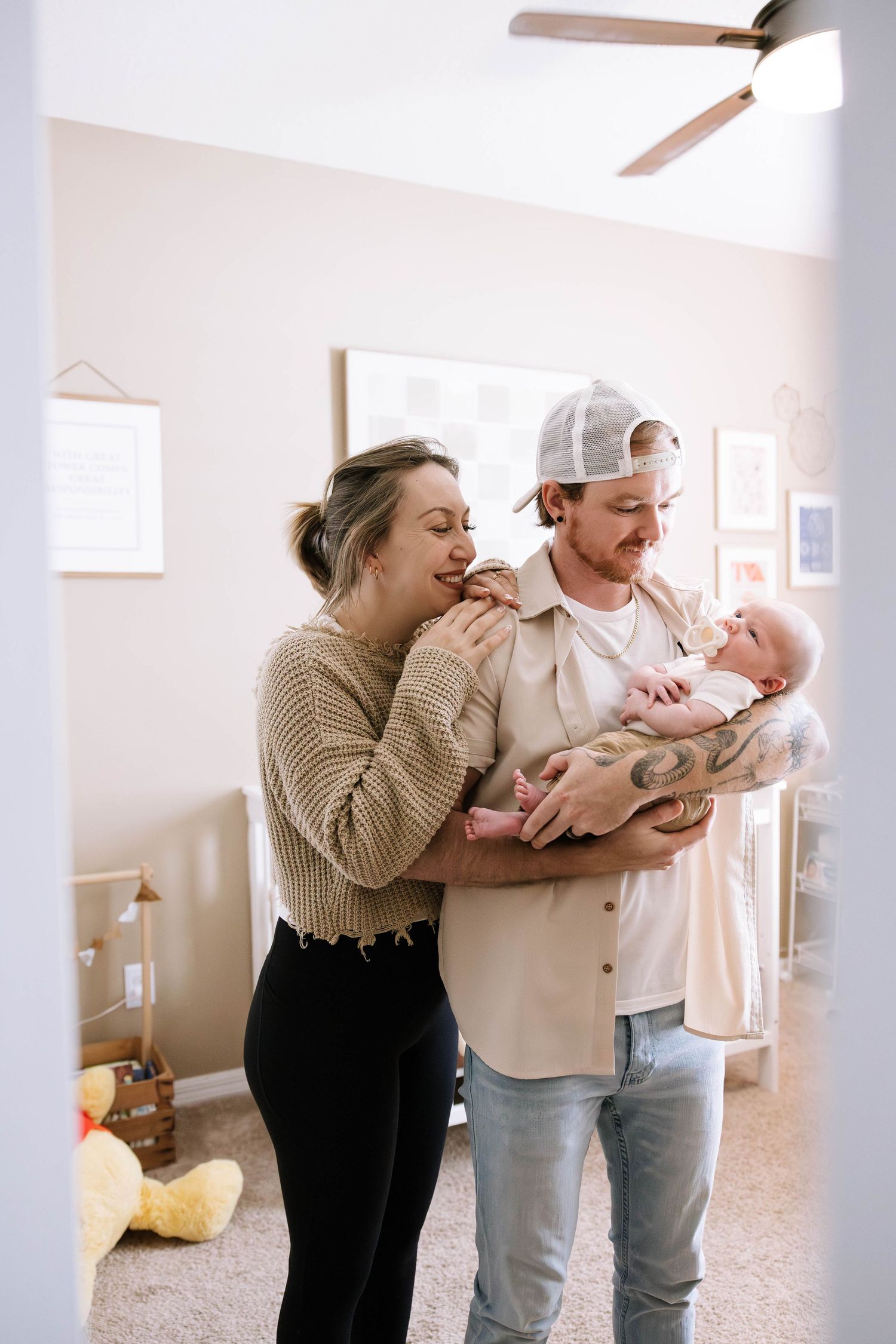 Happy young parents in a nursery smiling at their newborn baby held by the tattooed father. Home in Lakeland Florida.