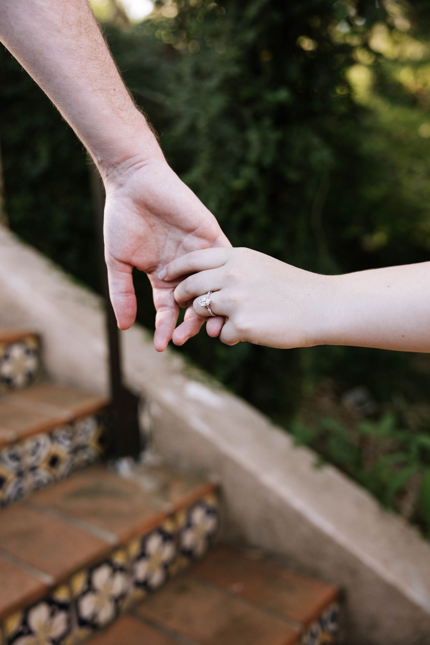 Close-up of couple holding hands on decorative tiled steps, woman wearing a sparkling diamond engagement ring.