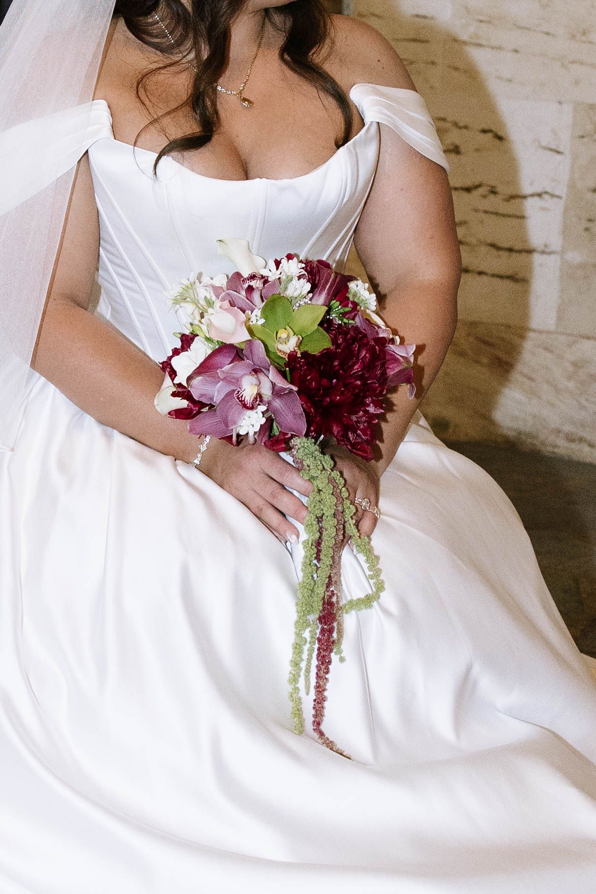 Bride in white off-shoulder gown holding a cascading burgundy and green wedding bouquet with trailing amaranthus.