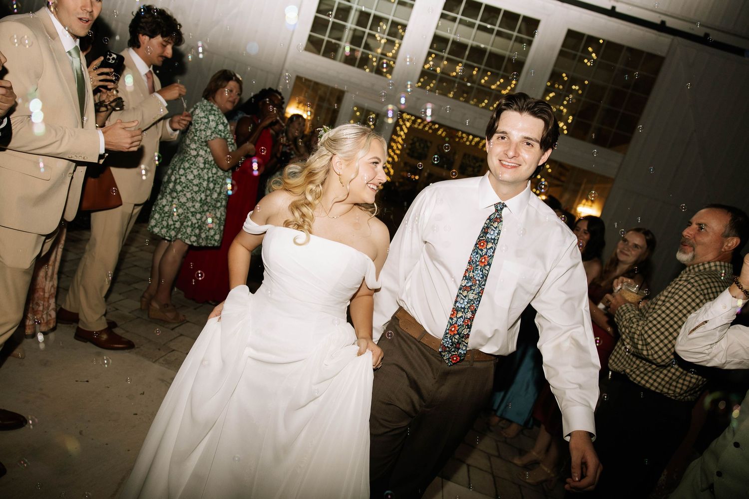 Bride and groom dancing joyfully at their wedding reception surrounded by guests in elegant attire.