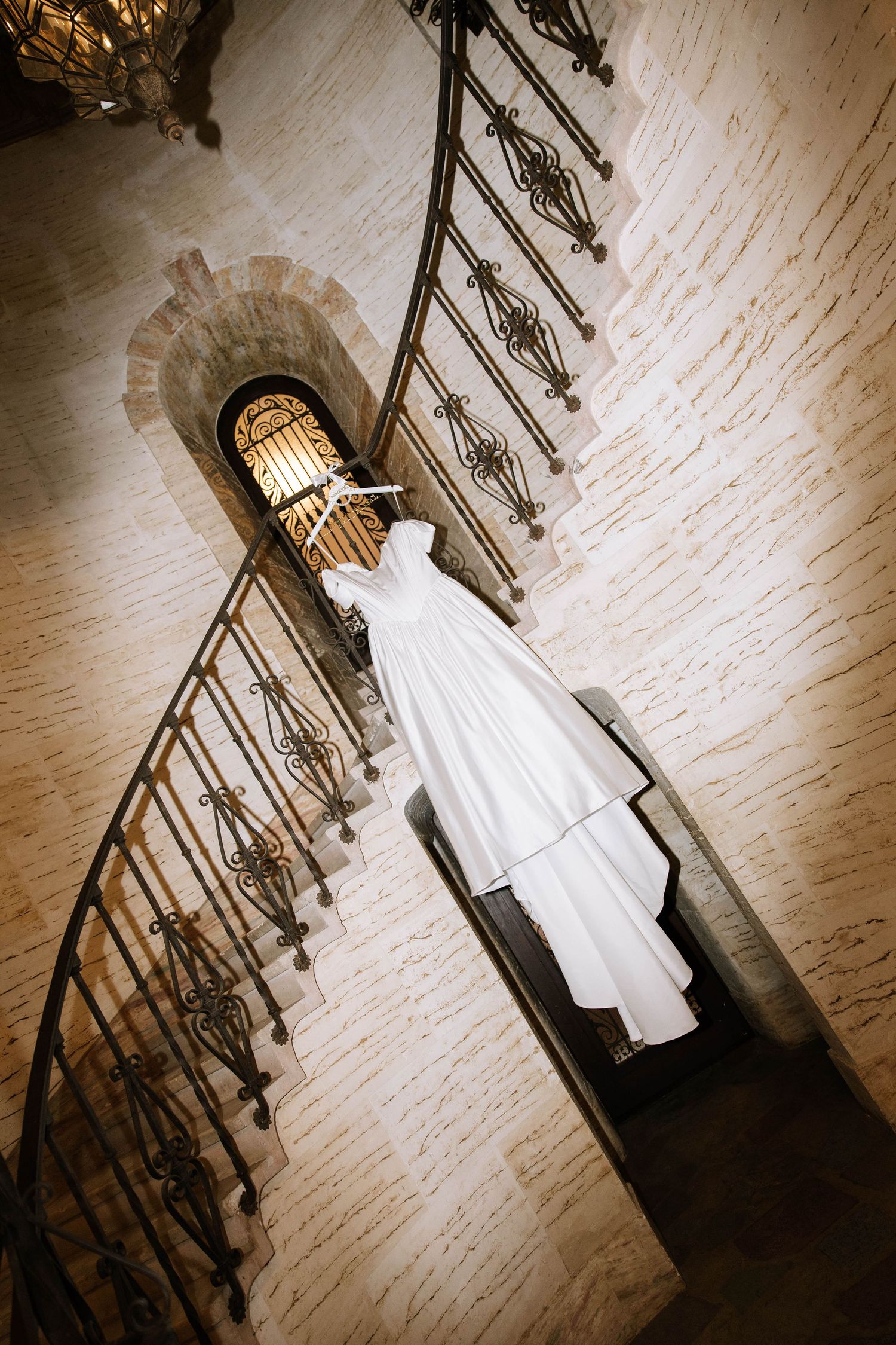 White wedding gown hanging on iron spiral staircase in stone tower.