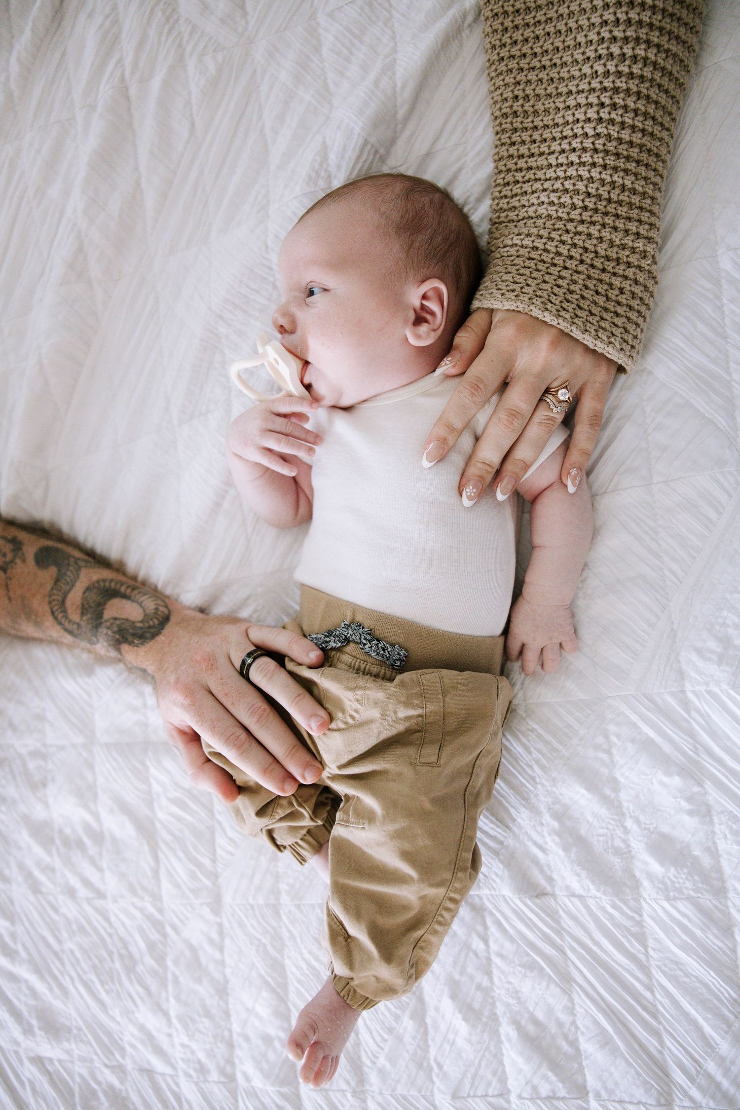 Overhead view of newborn baby with pacifier lying on white bed, gently held by parents hands. Home in Lakeland Florida.