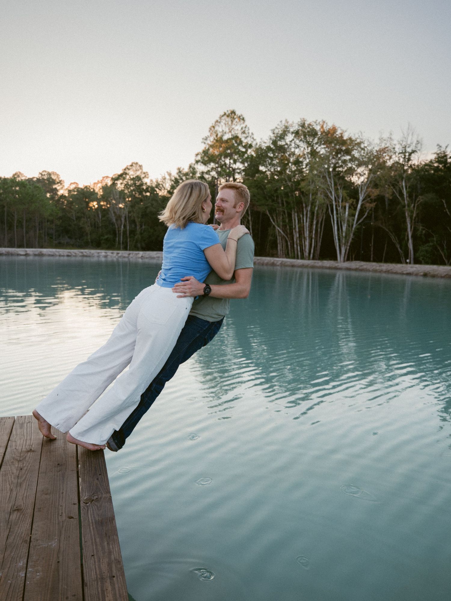 Happy couple embracing on a wooden dock at sunset beside a tranquil blue lake.