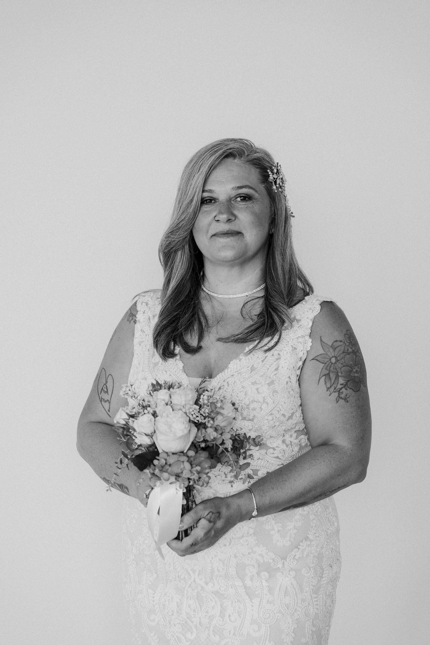 Black and white portrait of bride in lace gown holding bouquet against white background.
