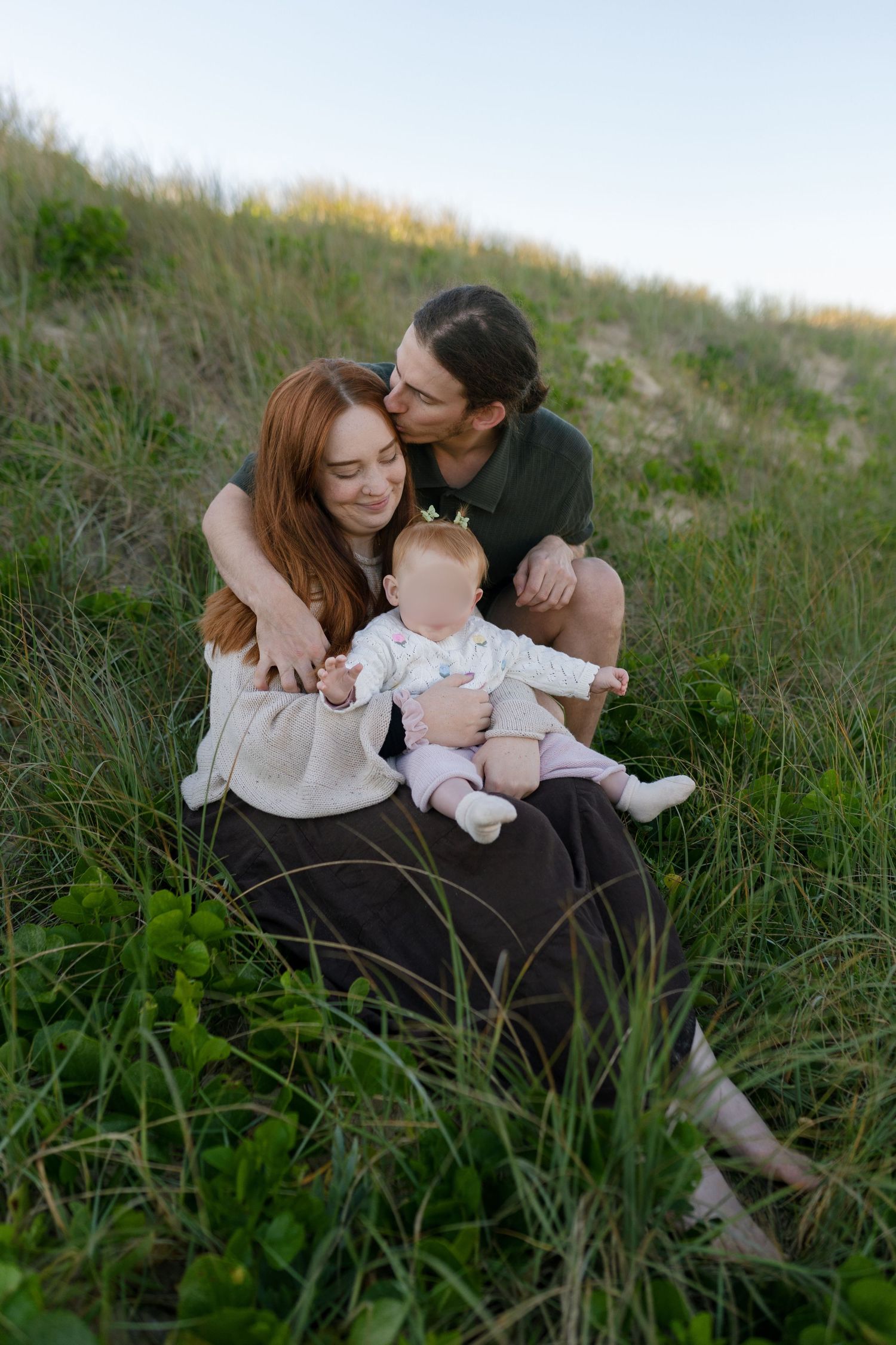 Family of three playing cuddling in the grass during a Sunshine Coast family photography session