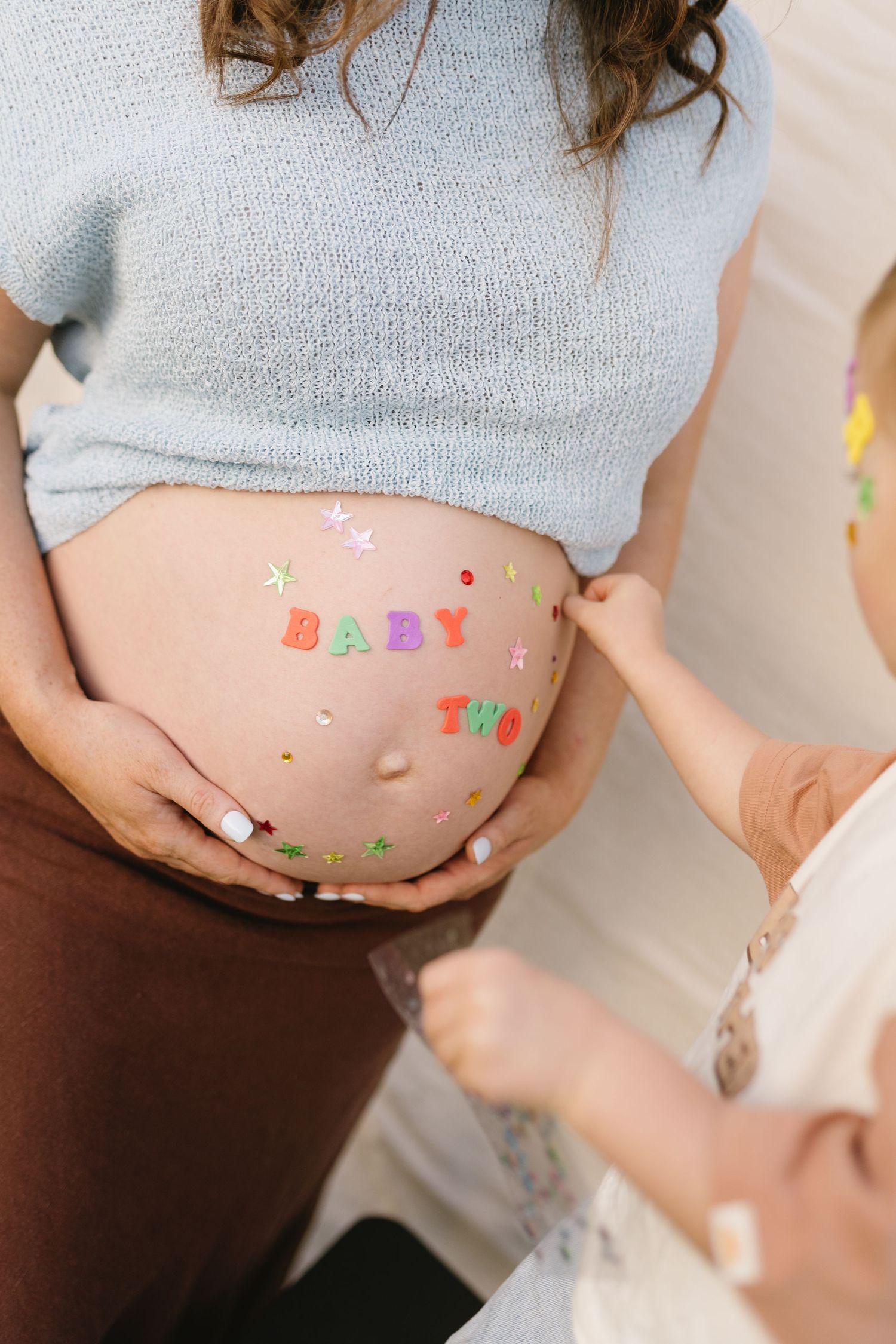 Pregnant mother playing with her toddler while he adds stickers to her belly