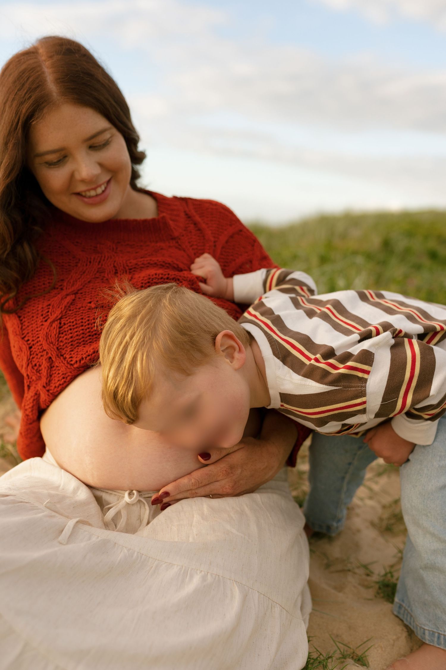 Pregnant mum laughing and playing with her toddler by the ocean