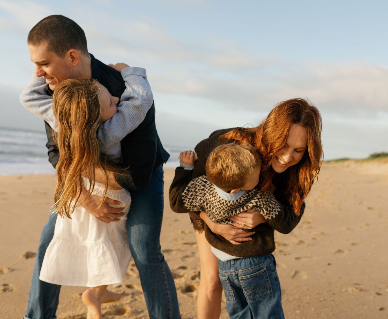 Family laughing together while playing along Warana Beach at sunrise