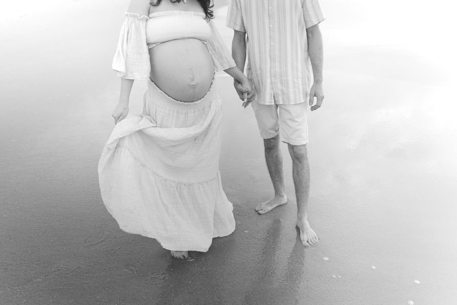 Expecting mother and father walking along the beach at sunset