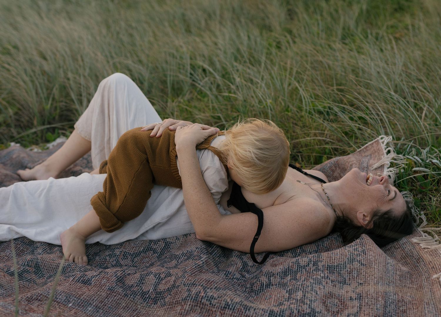 Mum cuddling and breastfeeding her baby surrounded by long grass