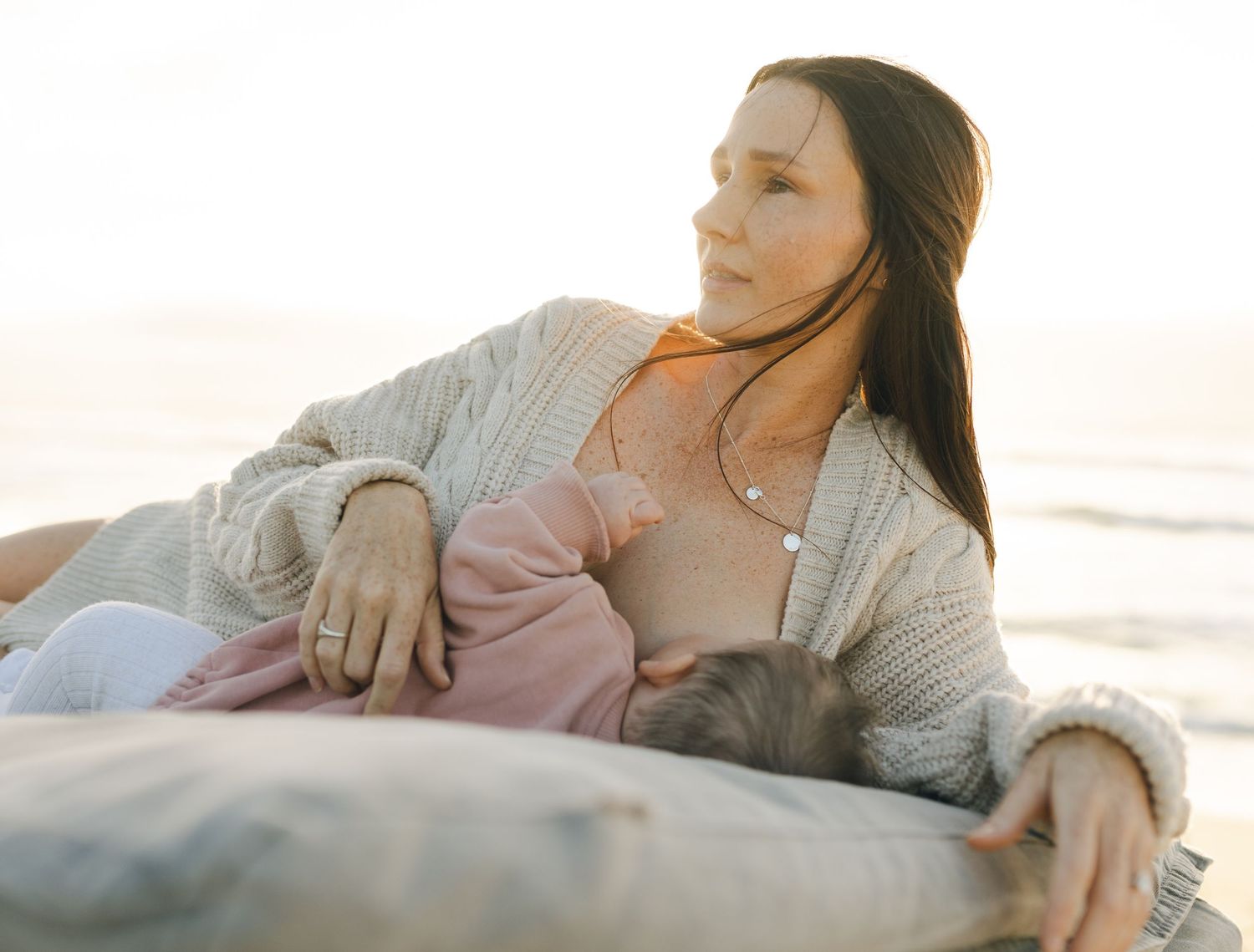 Mum and baby sharing a quiet breastfeeding moment by the ocean in winter