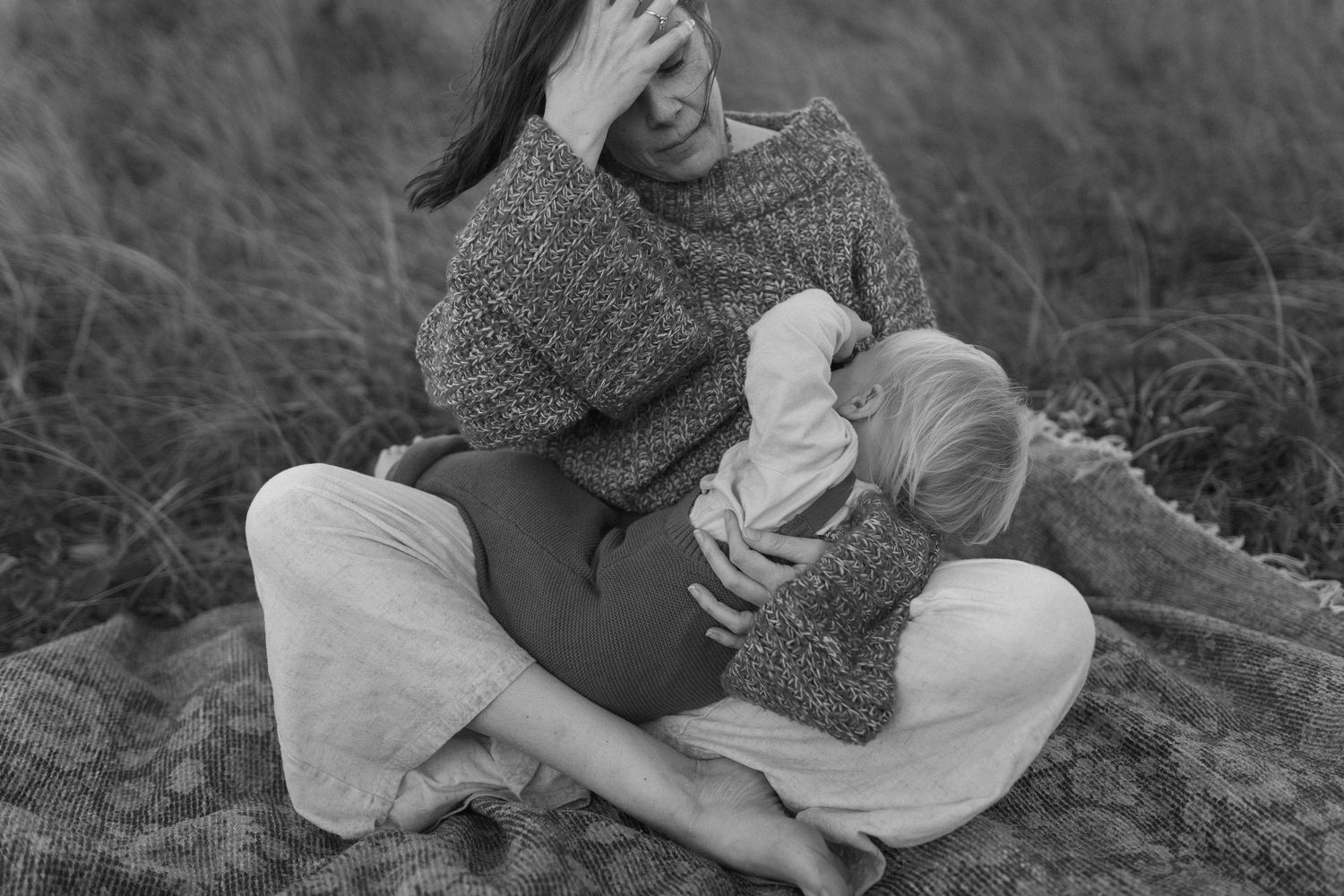 Mother breastfeeding her baby surrounded by long grass during a relaxed motherhood photography session