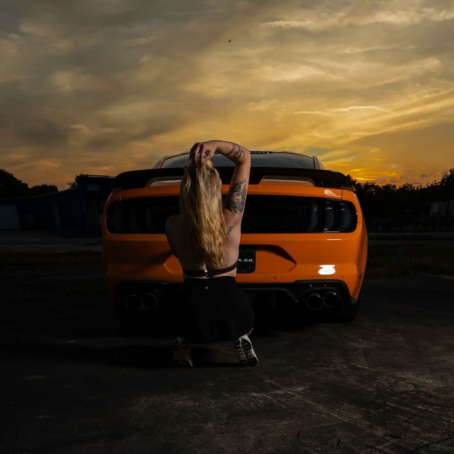 Cinematic creative portrait of a woman with an orange sports car at sunset