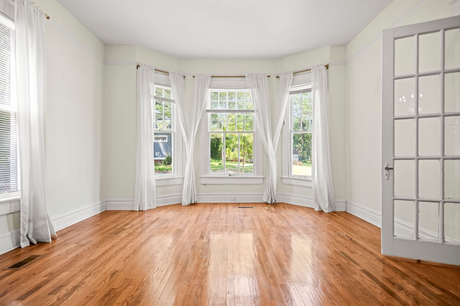 Professional Real Estate Photography of a bright empty room with bay windows, hardwood floors, and white walls showcasing natural light