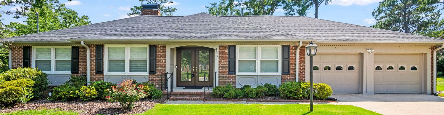 Single-story brick ranch house with beige siding, white trim, and attached two-car garage in a landscaped setting.